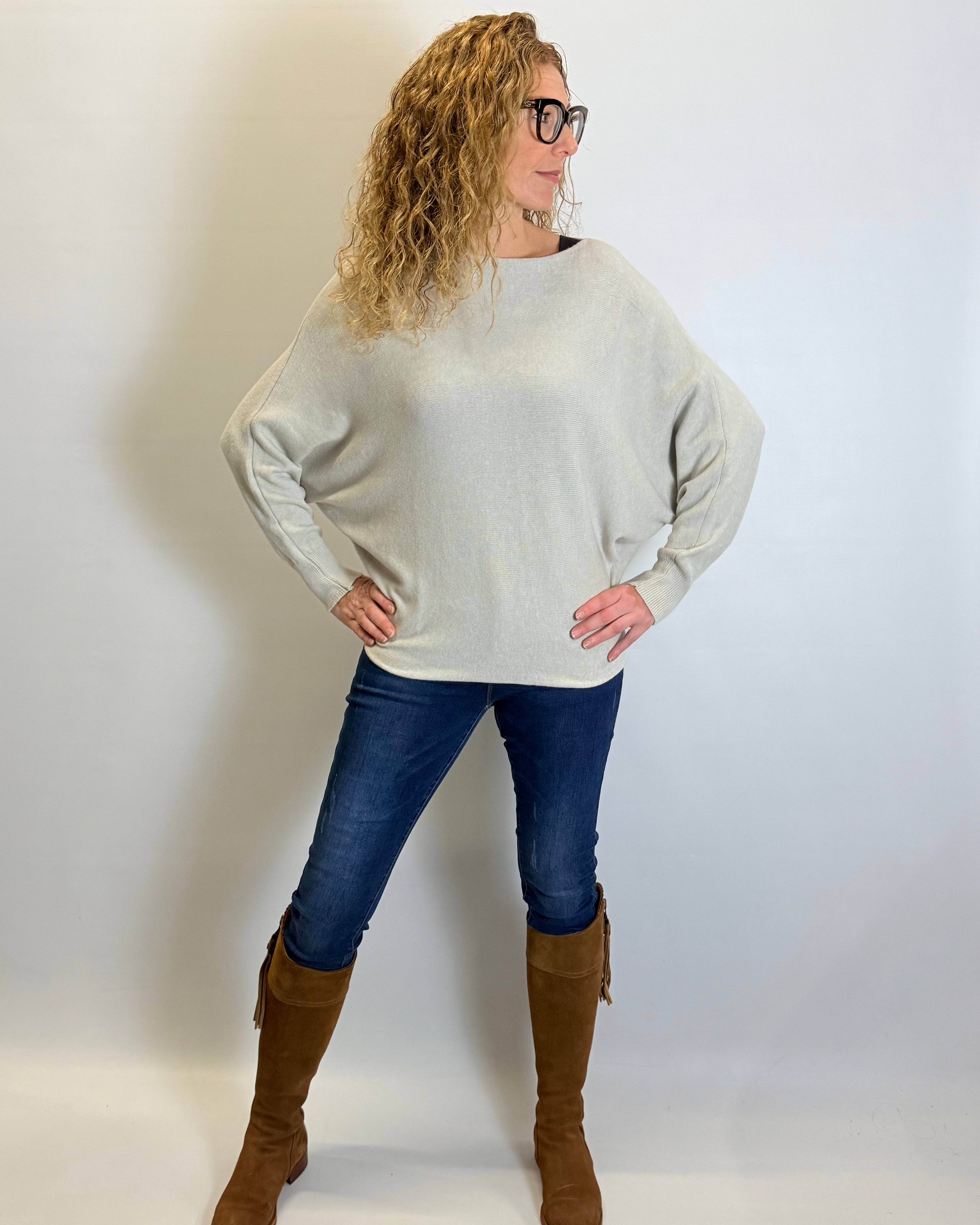 Woman wearing a light gray sweater, blue jeans, and brown knee-high boots against a white background