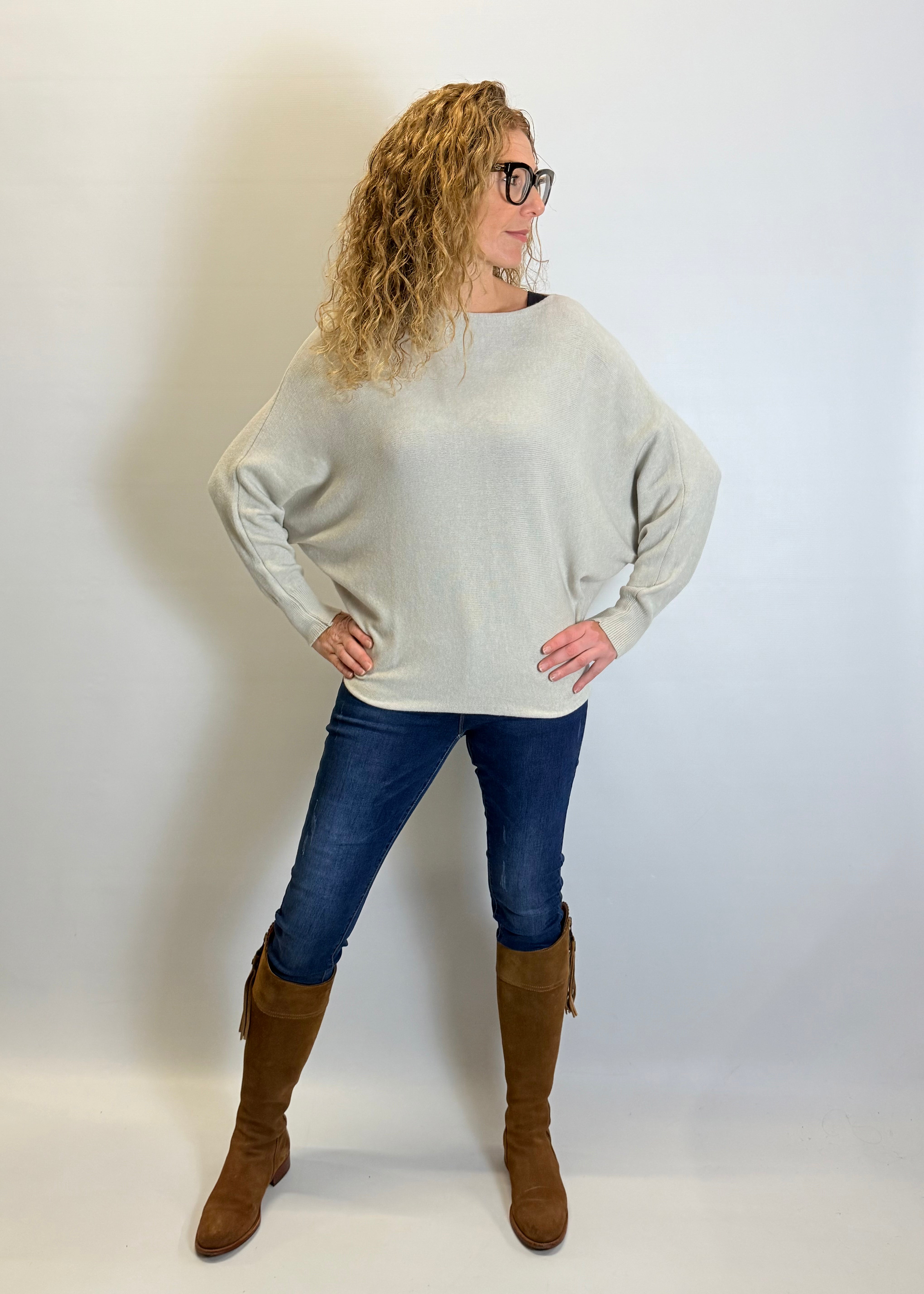 Woman wearing a light gray sweater, blue jeans, and brown knee-high boots against a white background