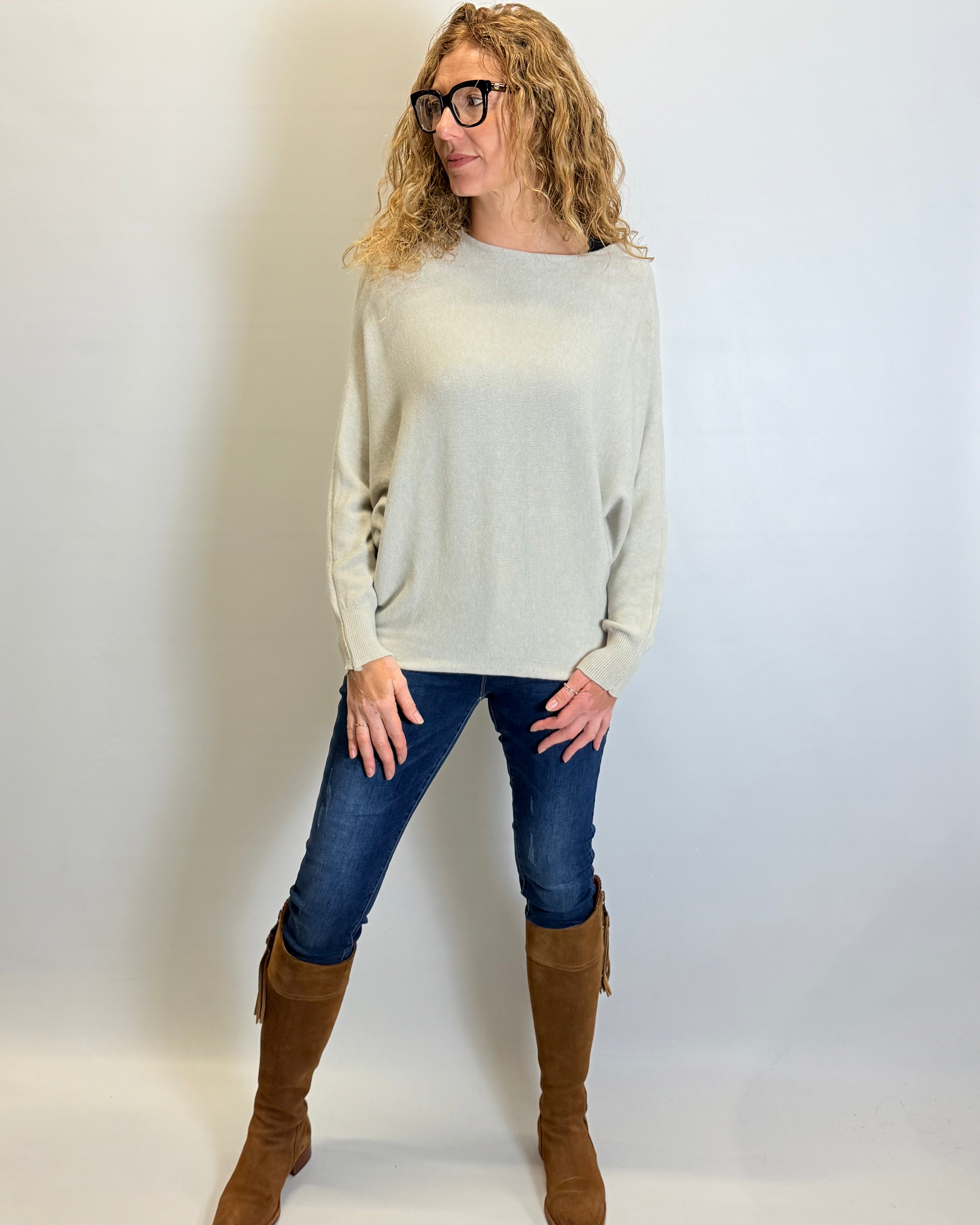 Woman wearing a light gray sweater, blue jeans, and brown knee-high boots against a white background