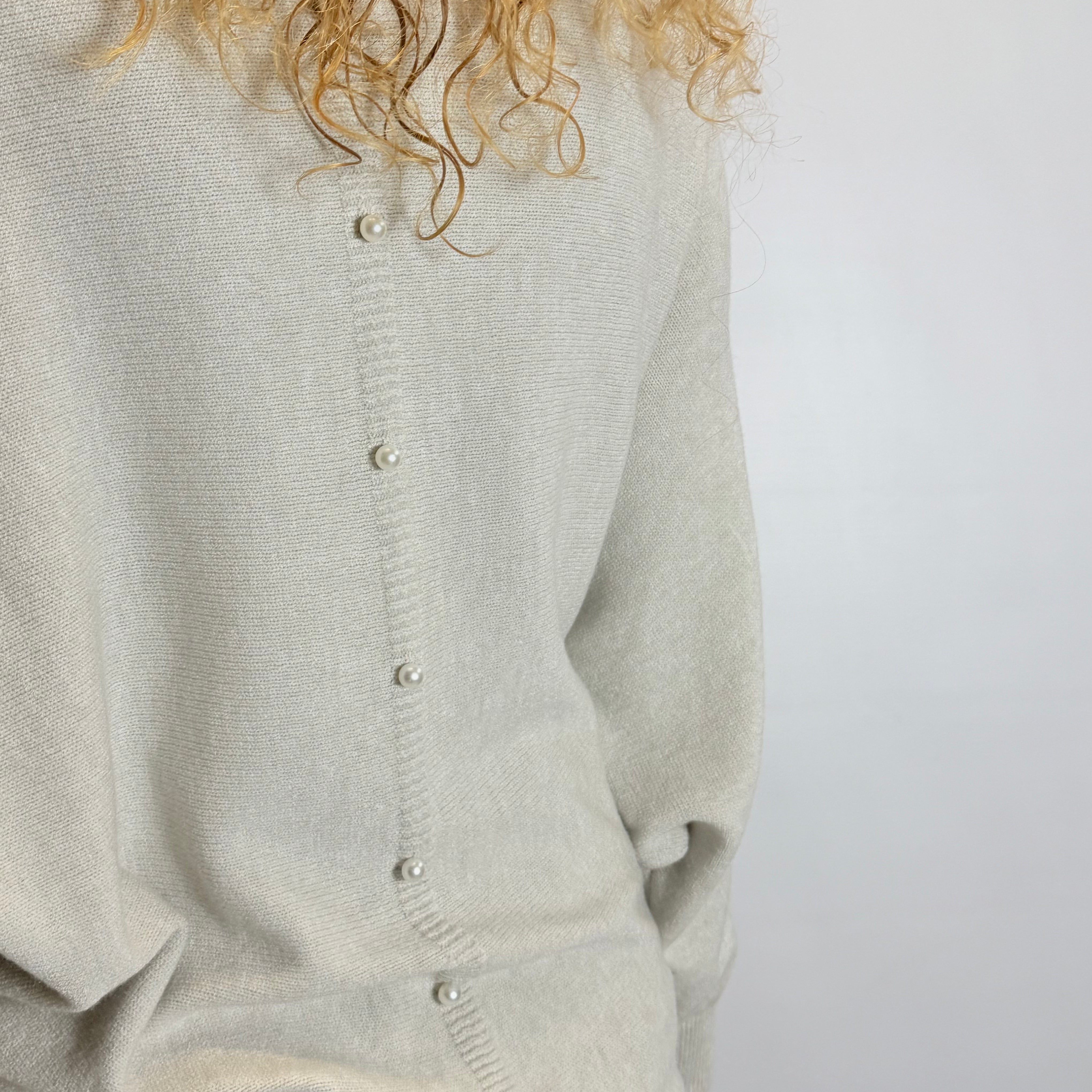 Light gray cardigan worn by a person with curly hair on a white background