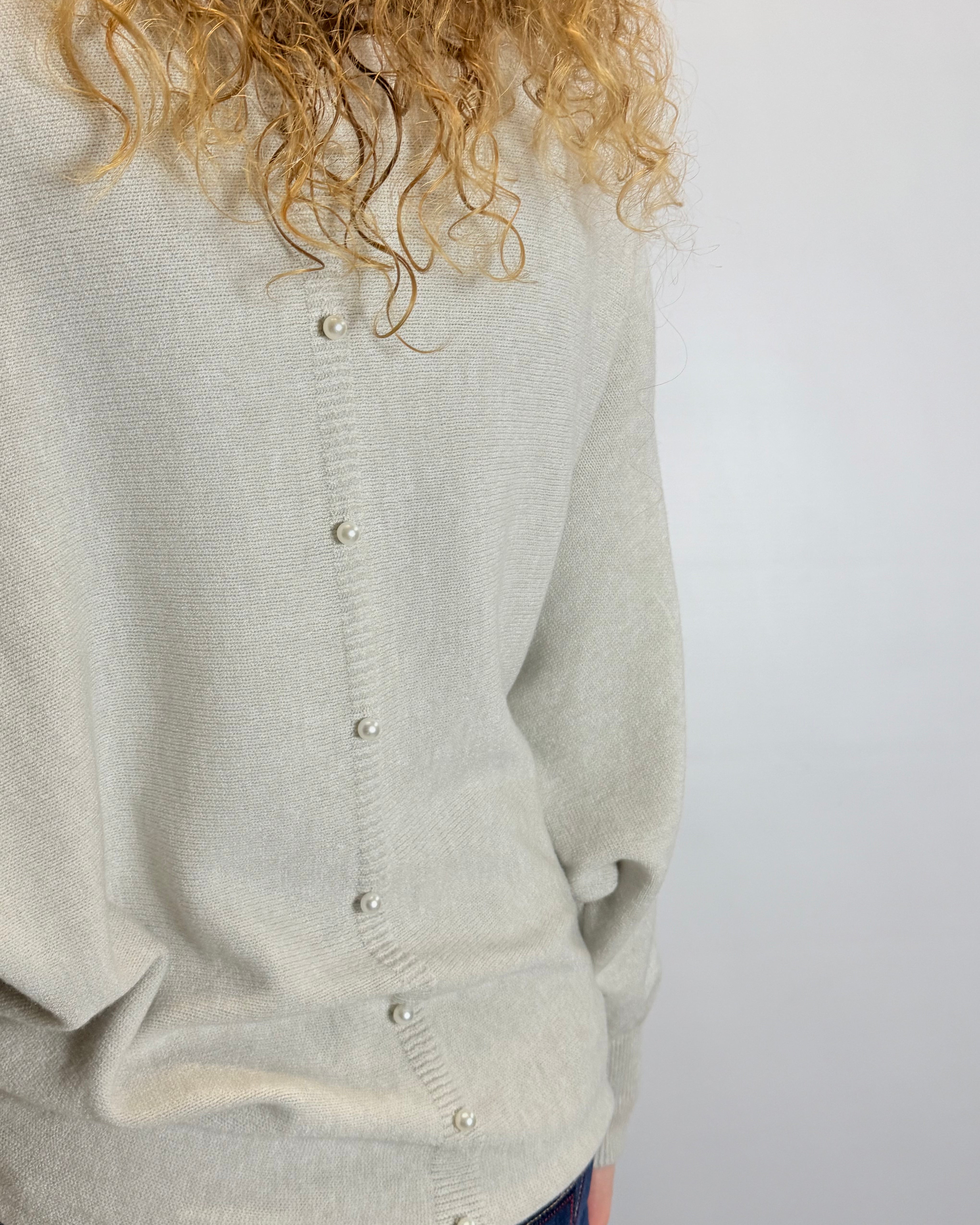Light gray cardigan worn by a person with curly hair on a white background