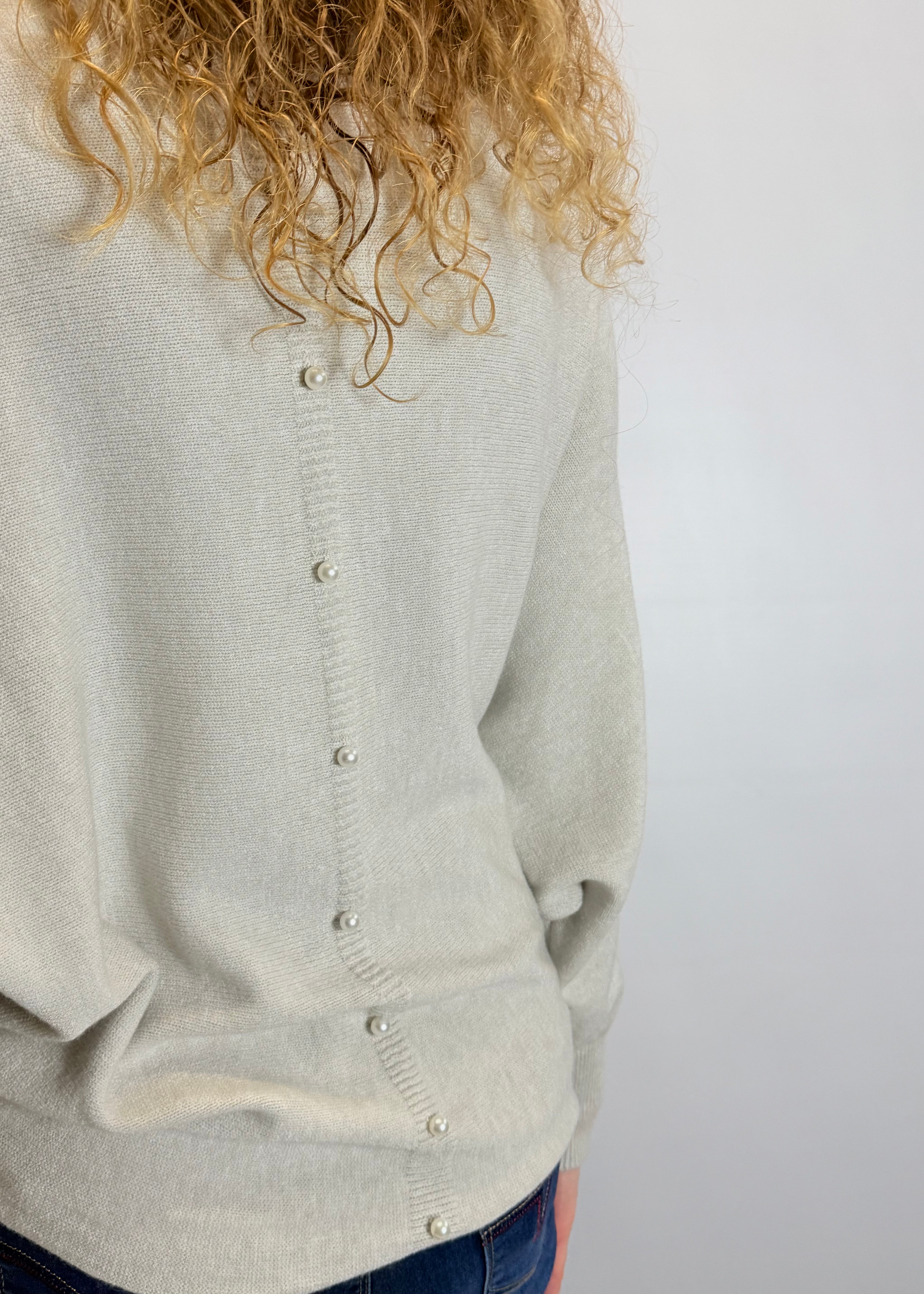 Light gray cardigan worn by a person with curly hair on a white background