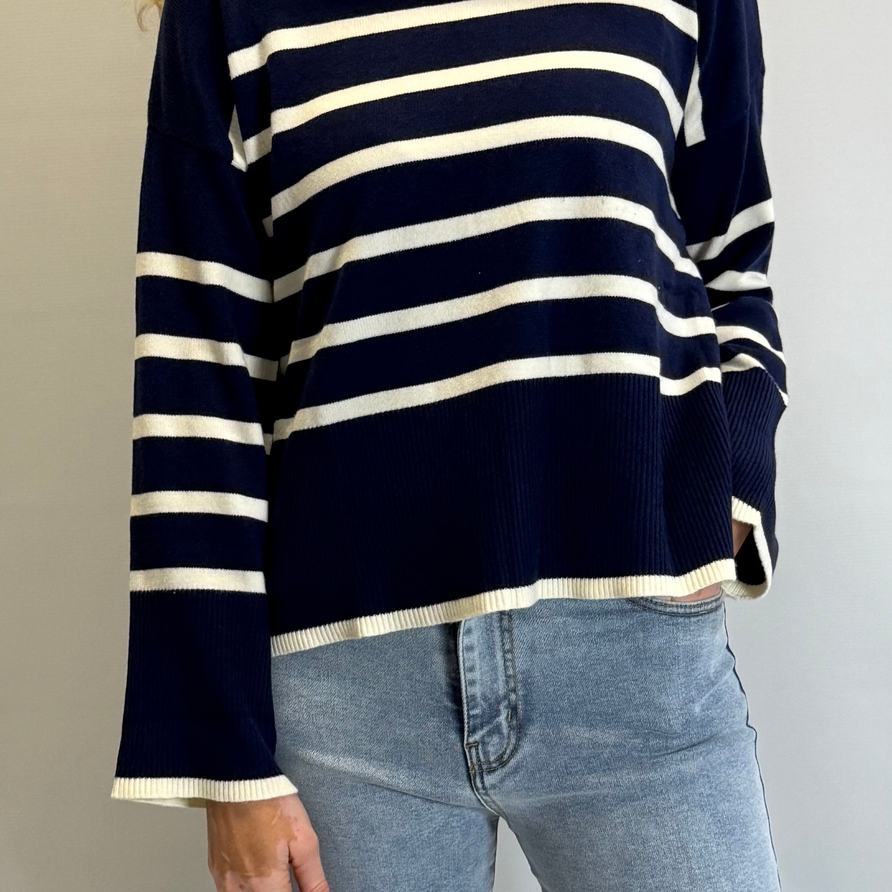 Person wearing a navy and white striped sweater with blue jeans against a plain background