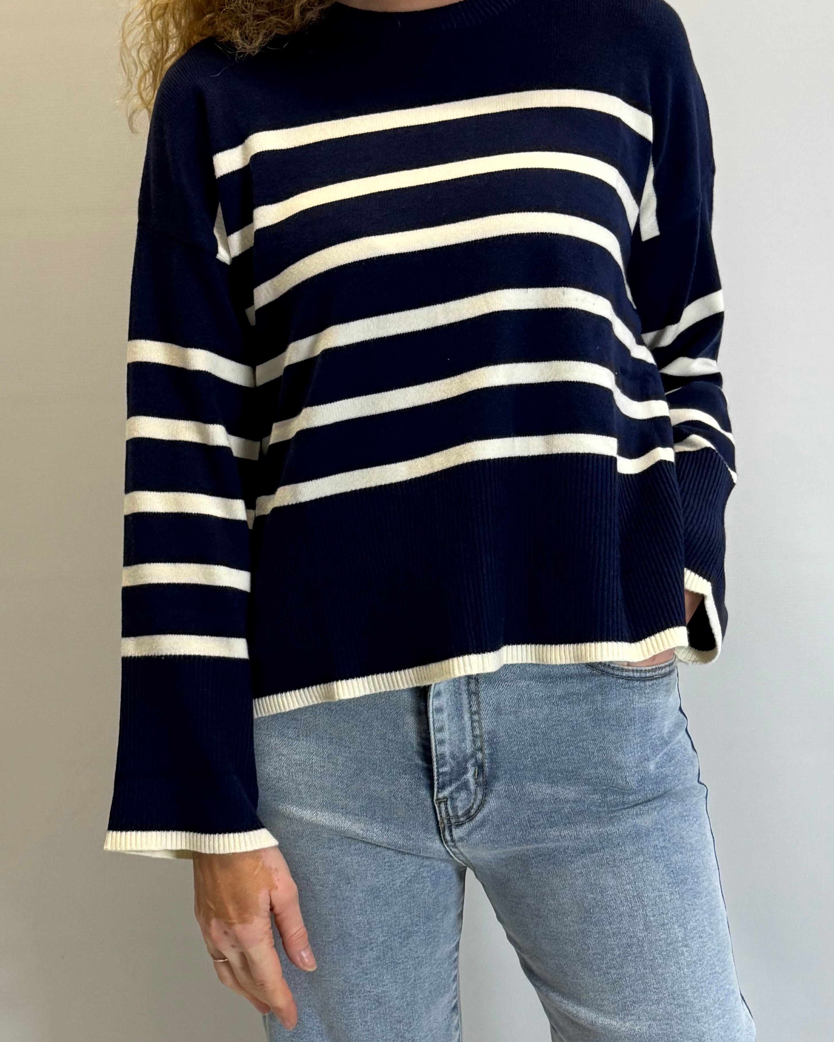 Person wearing a navy and white striped sweater with blue jeans against a plain background