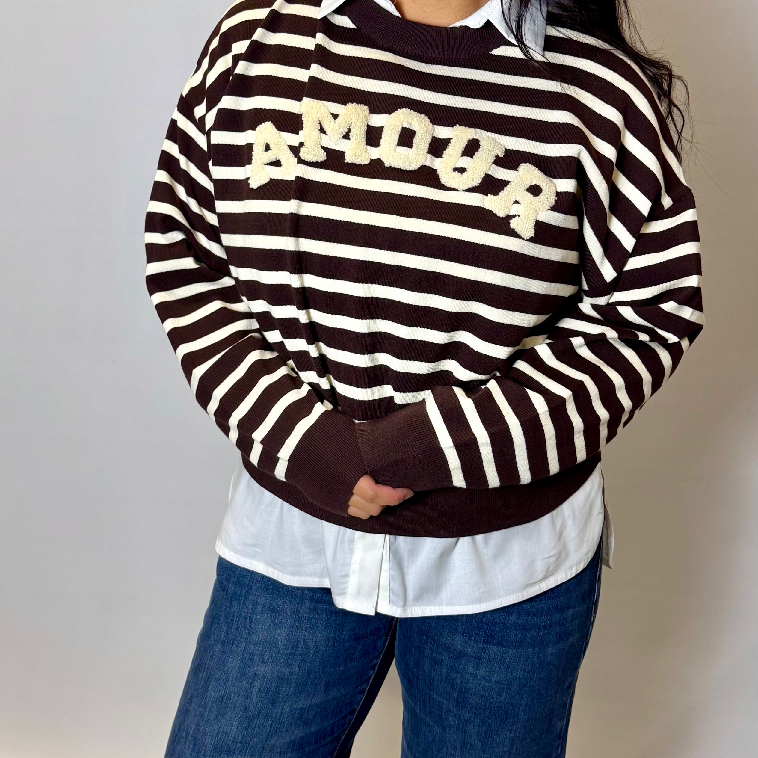 Person wearing a black and white striped sweater with 'MOOP' text, white shirt, and blue jeans against a plain background.