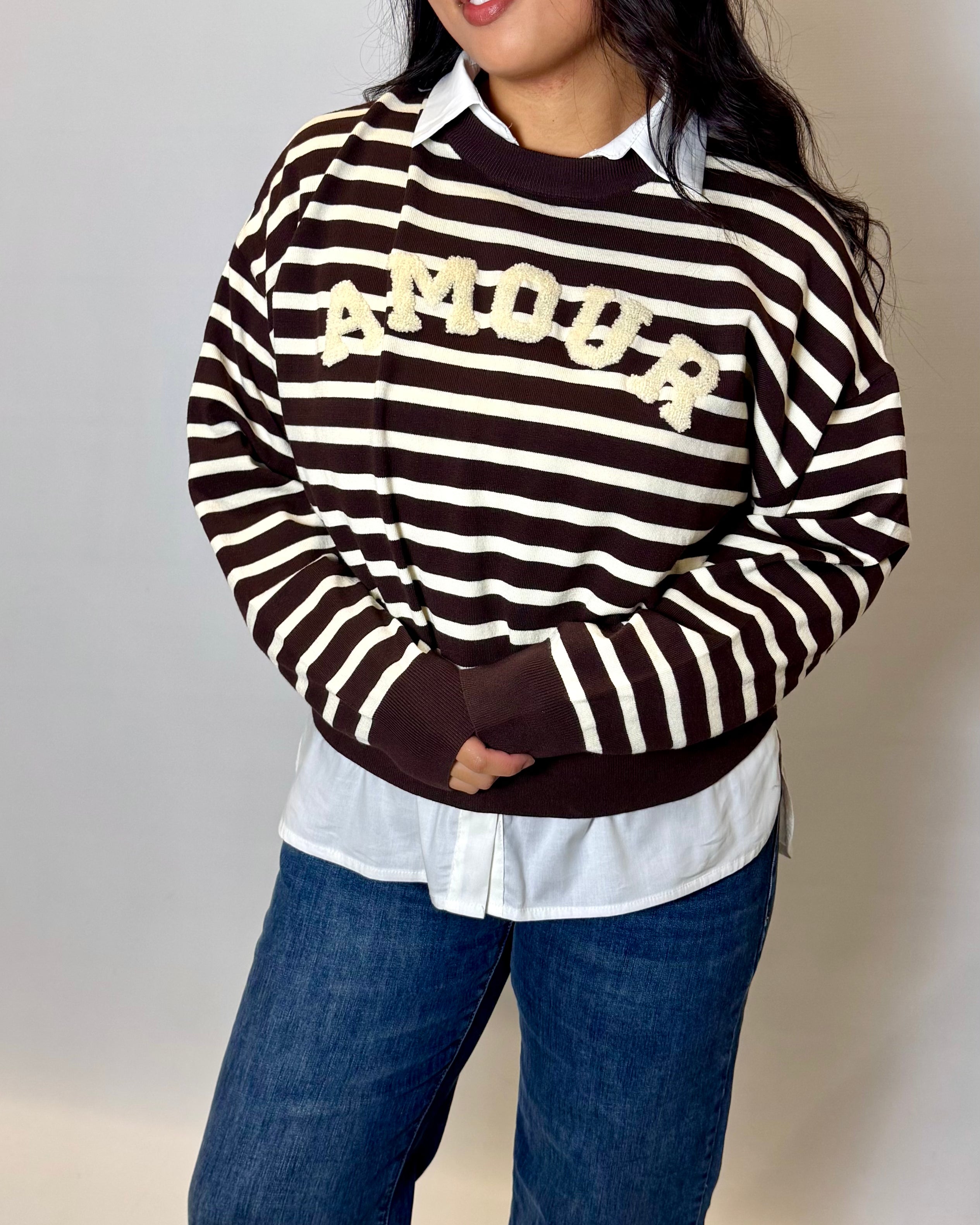 Person wearing a black and white striped sweater with 'MOOP' text, white shirt, and blue jeans against a plain background.