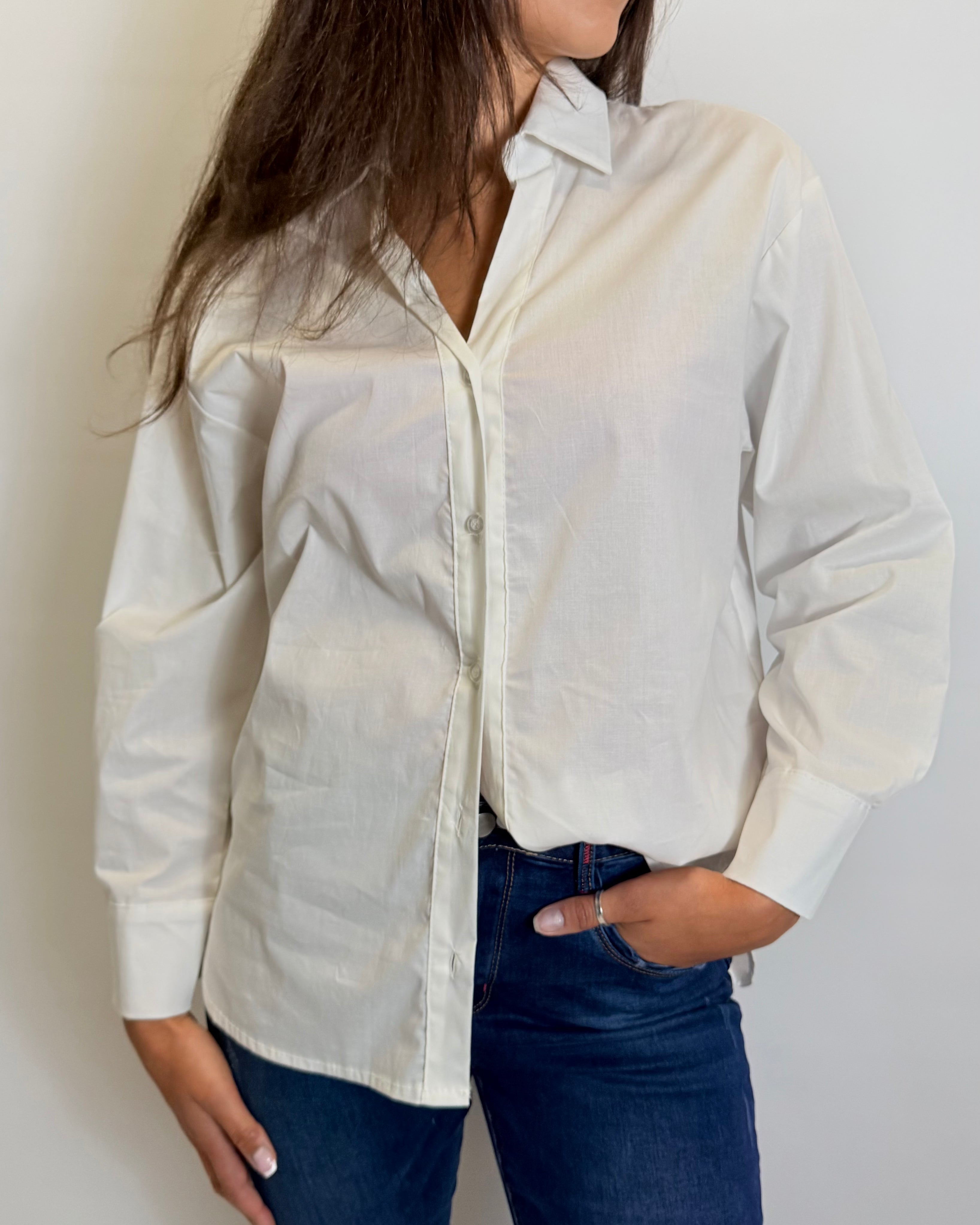 Person wearing a light-colored button-up shirt and dark jeans against a plain background