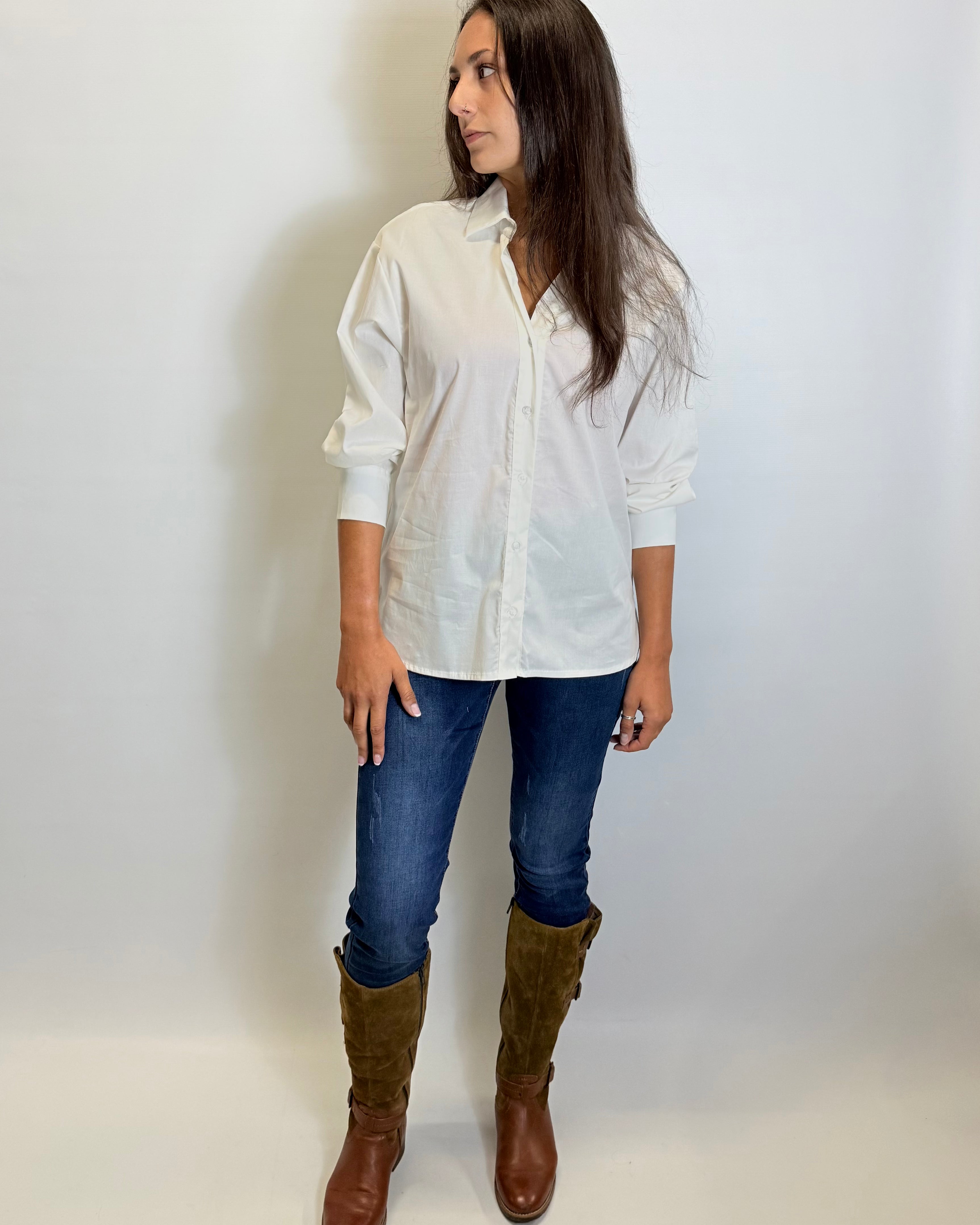 Woman wearing a white shirt, blue jeans, and brown boots against a plain background