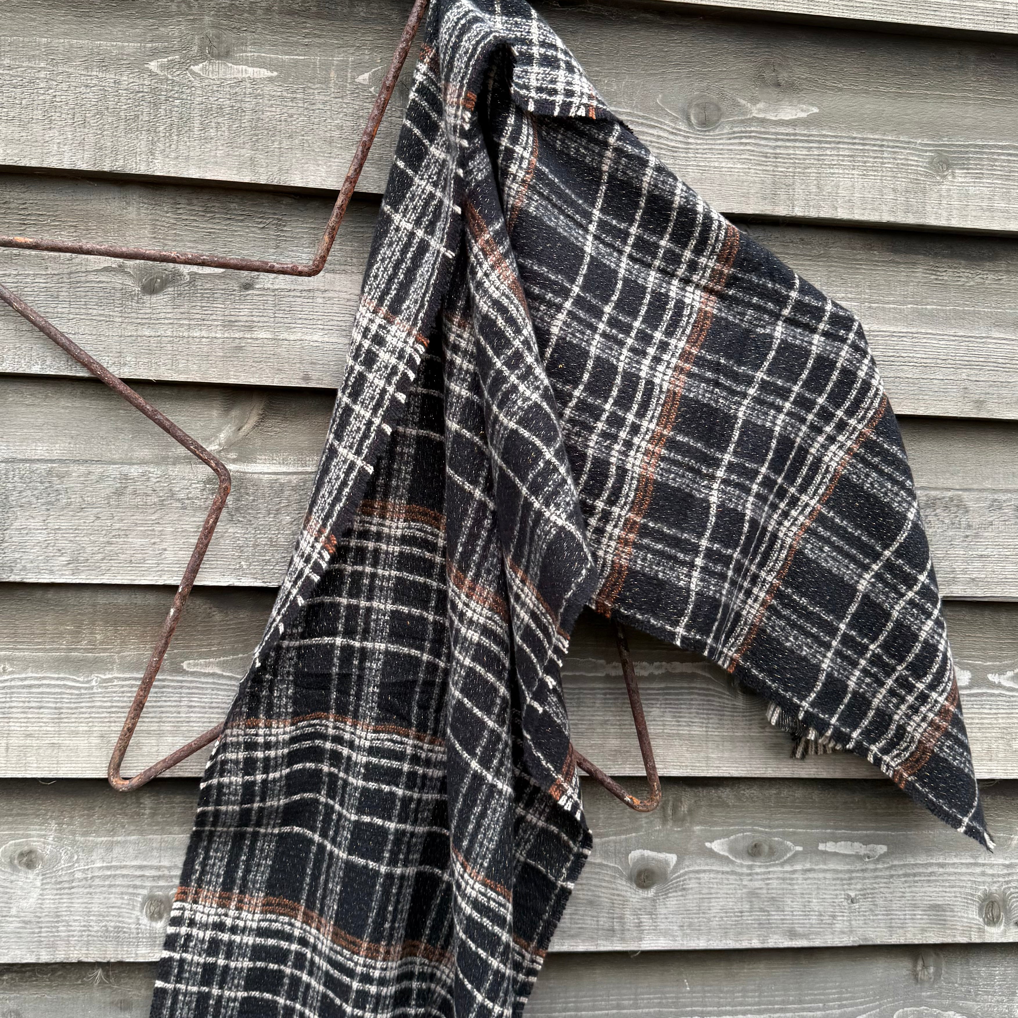 Plaid blanket draped over a metal frame against a wooden wall