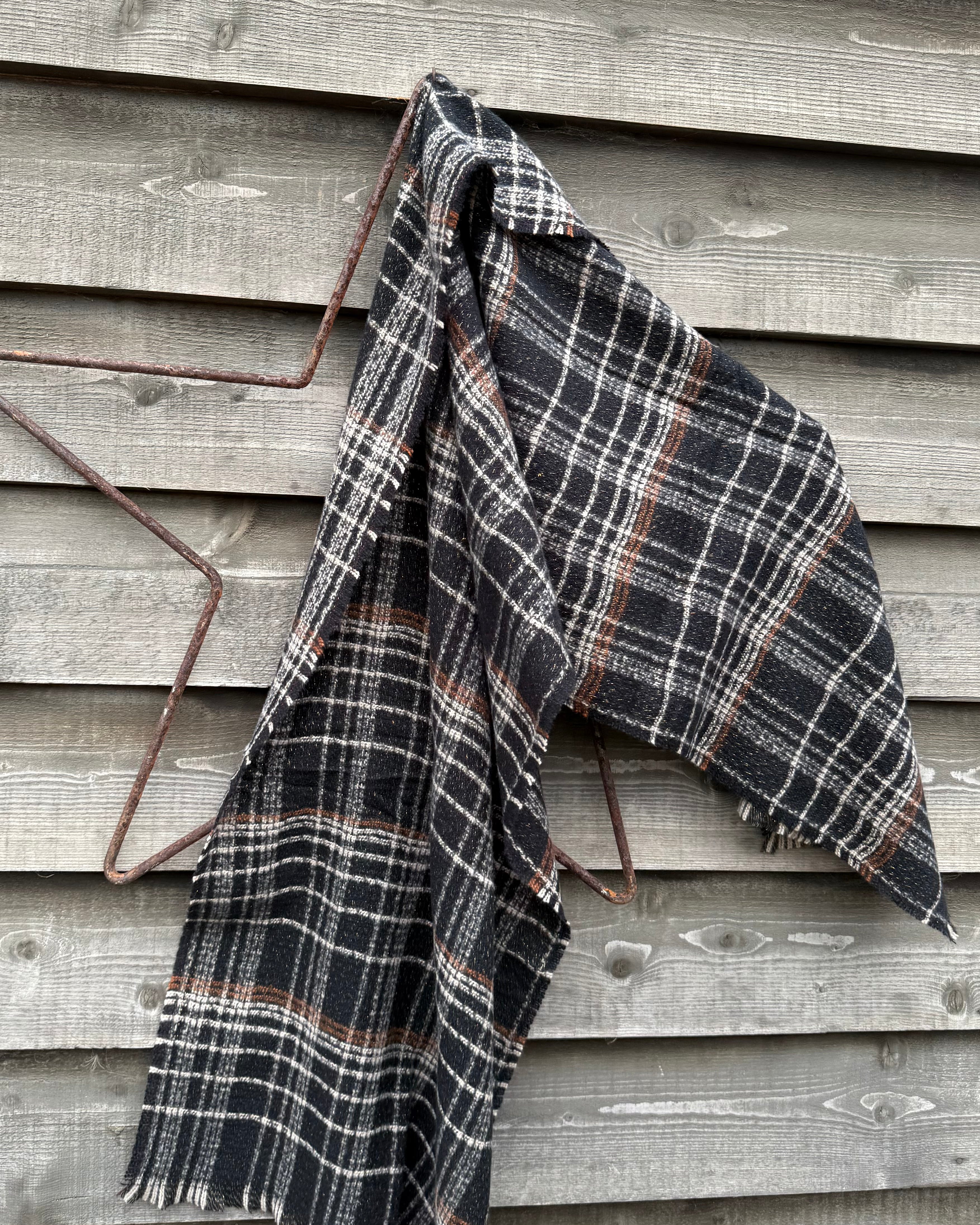Plaid blanket draped over a metal frame against a wooden wall