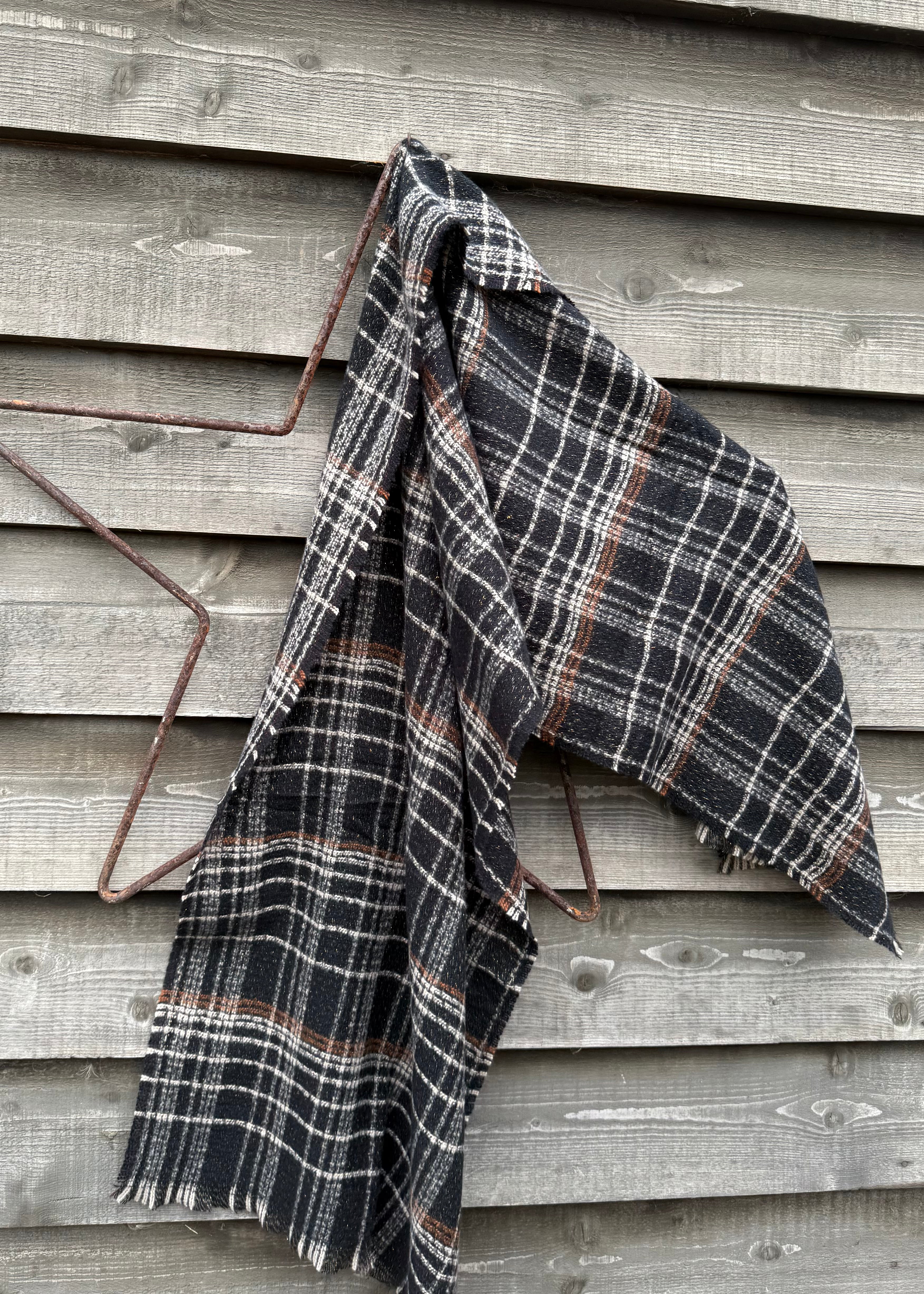 Plaid blanket draped over a metal frame against a wooden wall