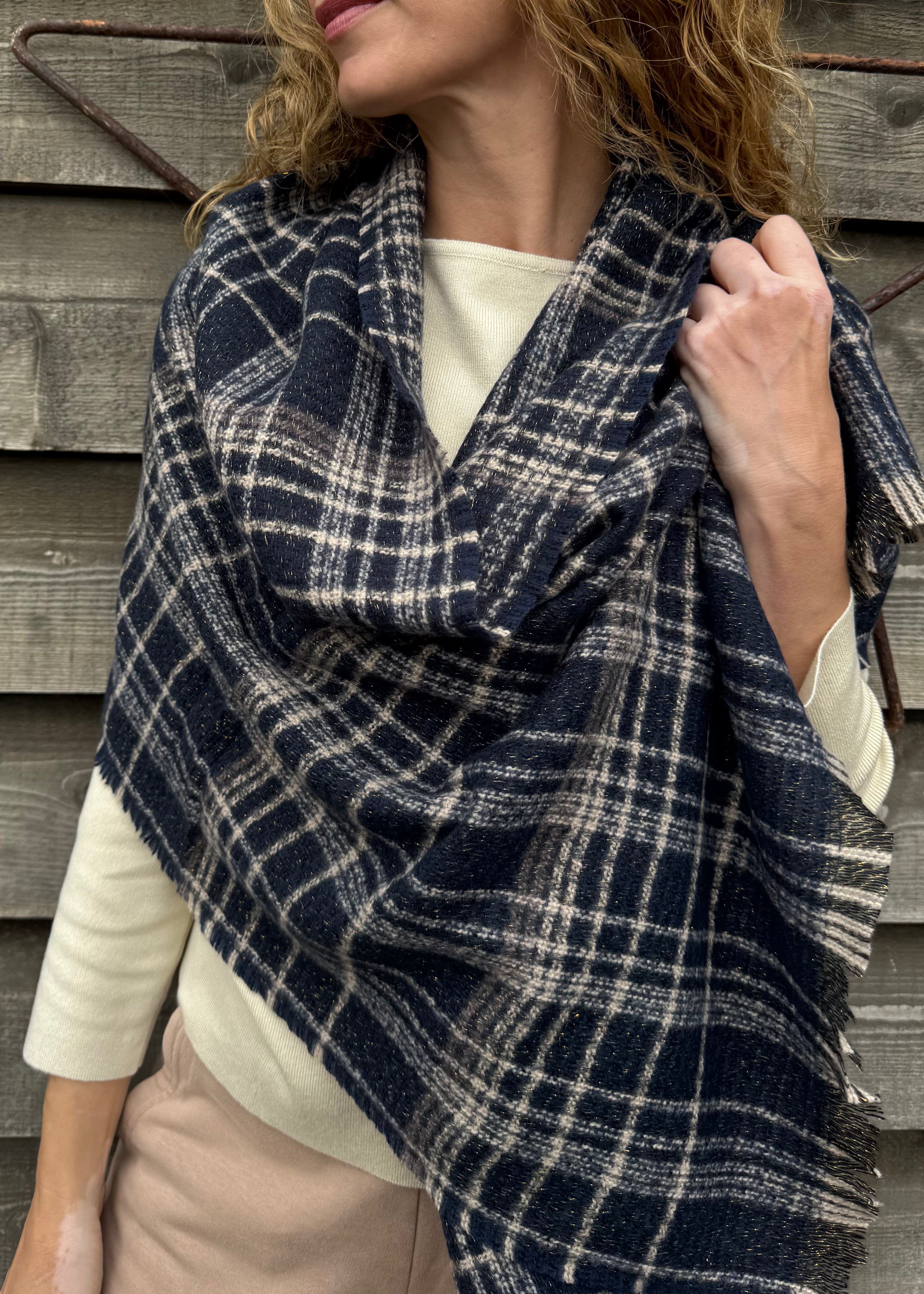 Woman wearing a blue and white plaid scarf against a wooden wall.