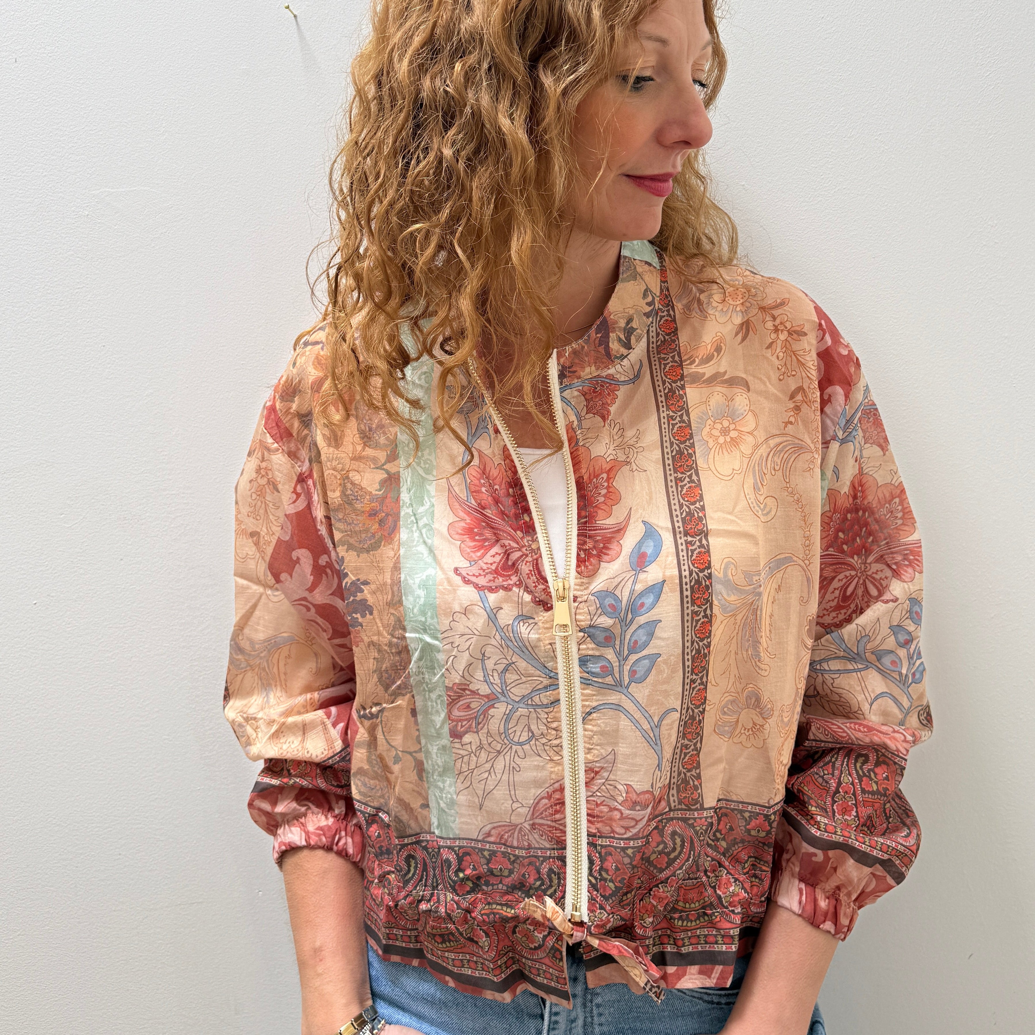 Woman wearing a patterned jacket and jeans against a plain background