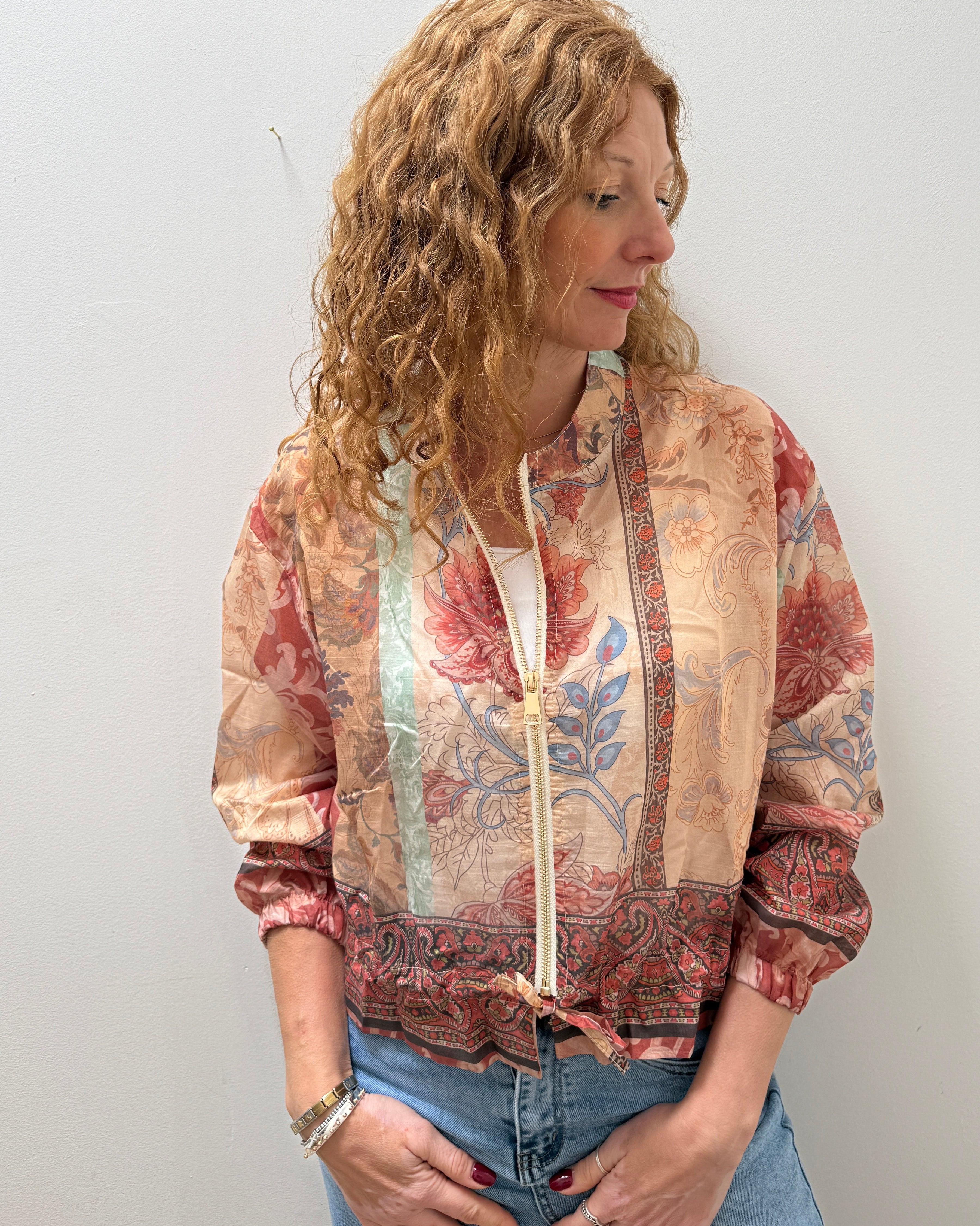 Woman wearing a patterned jacket and jeans against a plain background