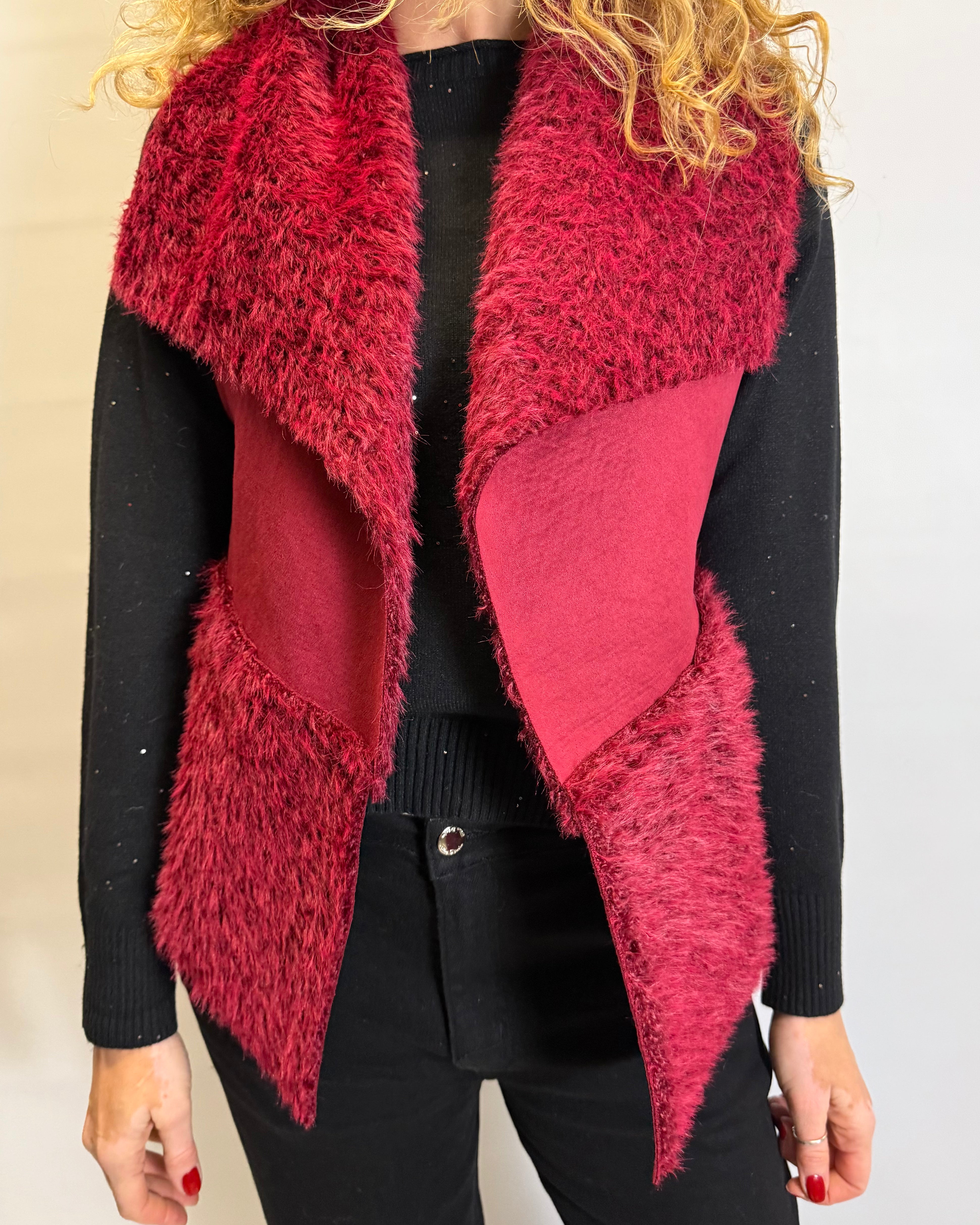 Person wearing a red furry vest over a black outfit against a plain background