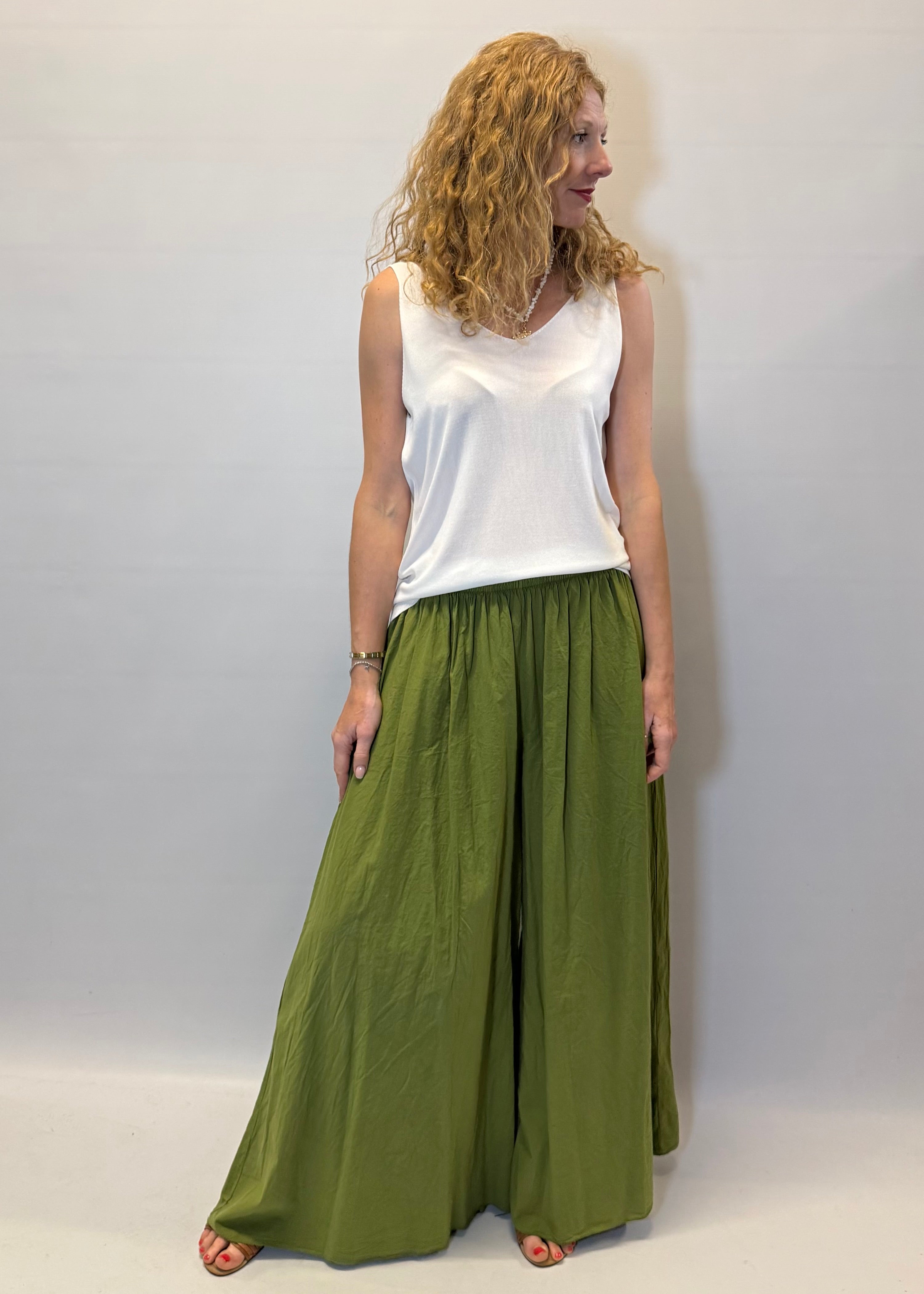 Woman wearing a white top and green wide-leg pants against a plain background