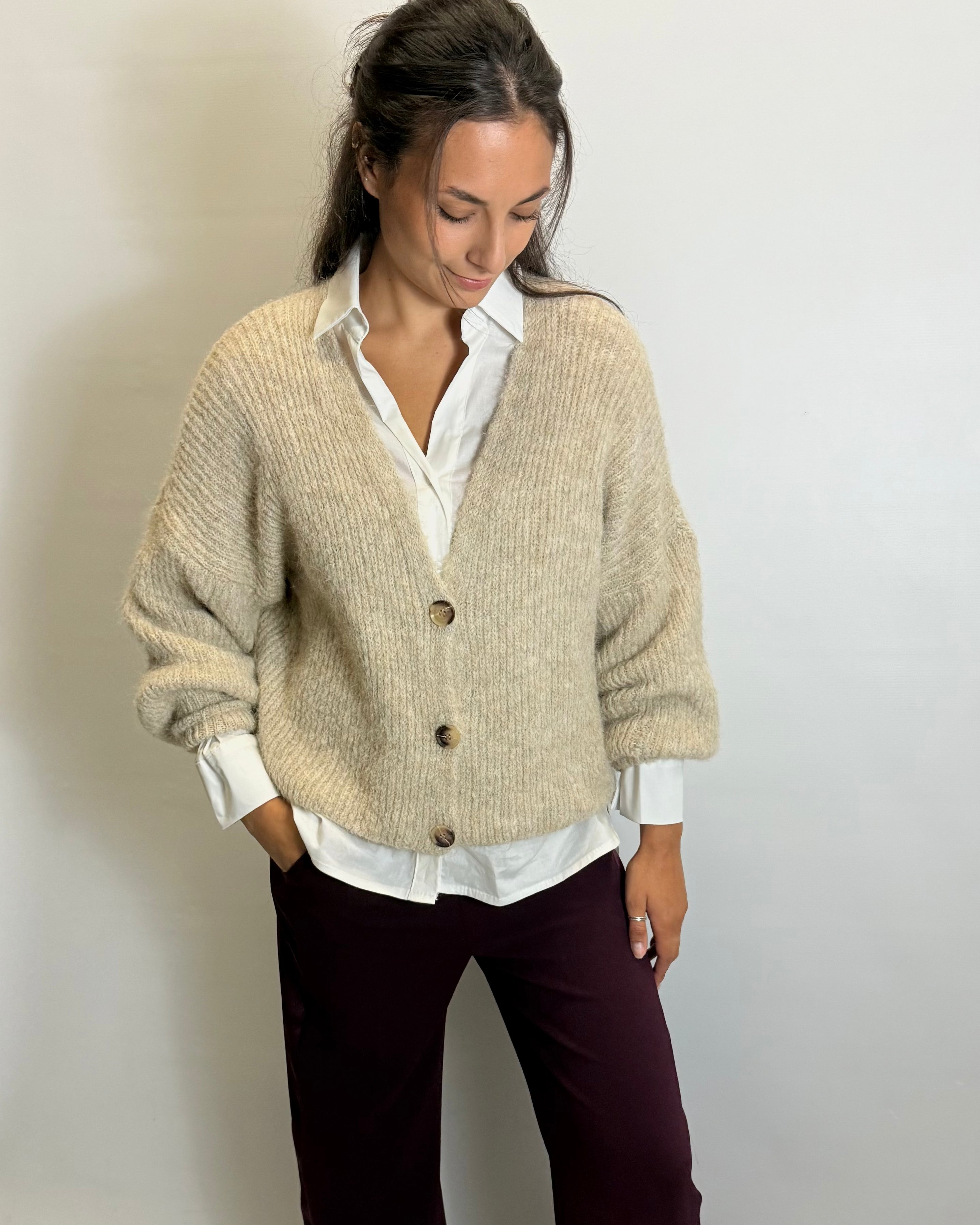 Woman wearing a beige cardigan over a white shirt with a plain background