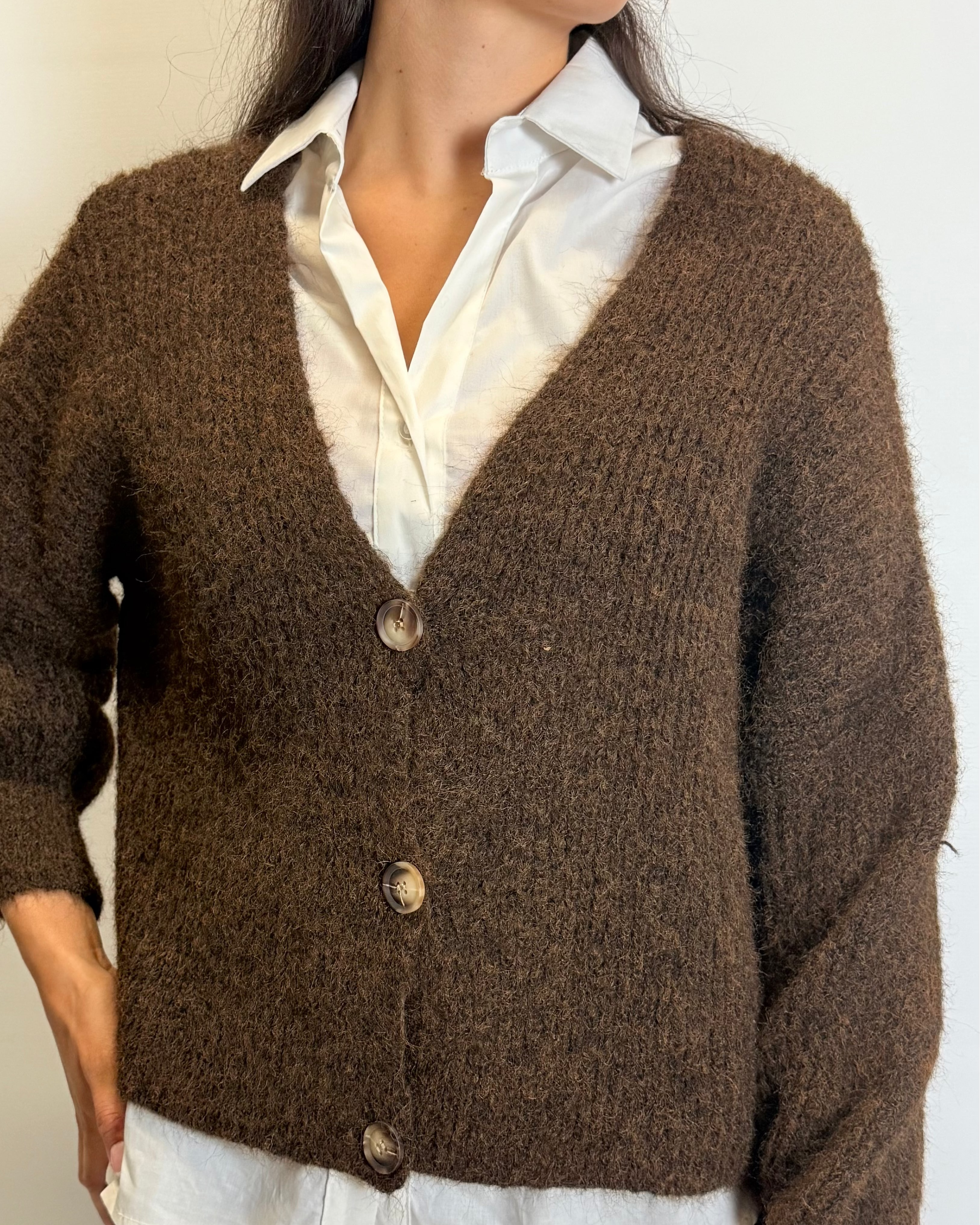 Person wearing a brown cardigan over a white shirt with a neutral background