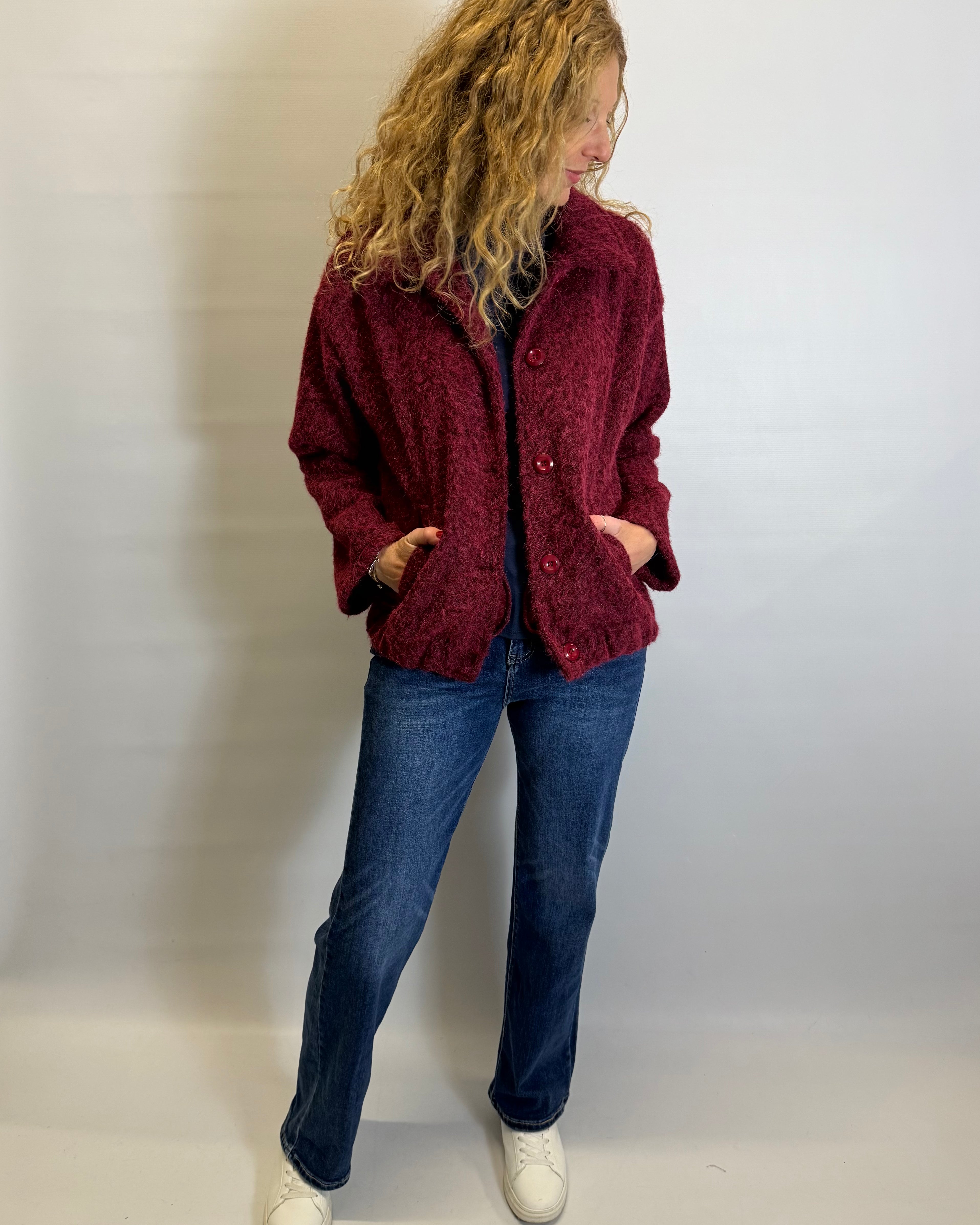 Person wearing a red jacket and blue jeans against a plain background