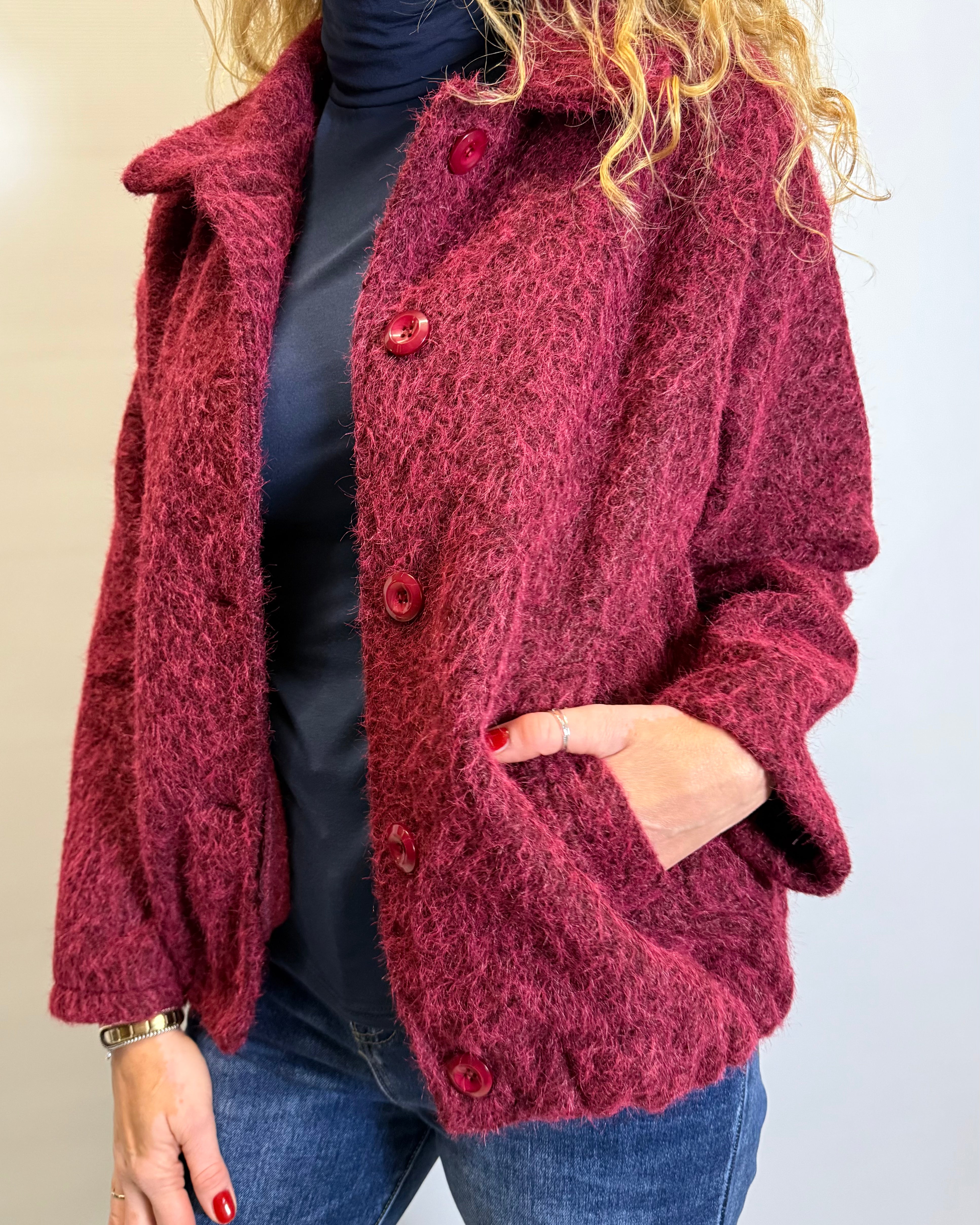 Person wearing a red textured jacket with buttons on a plain background