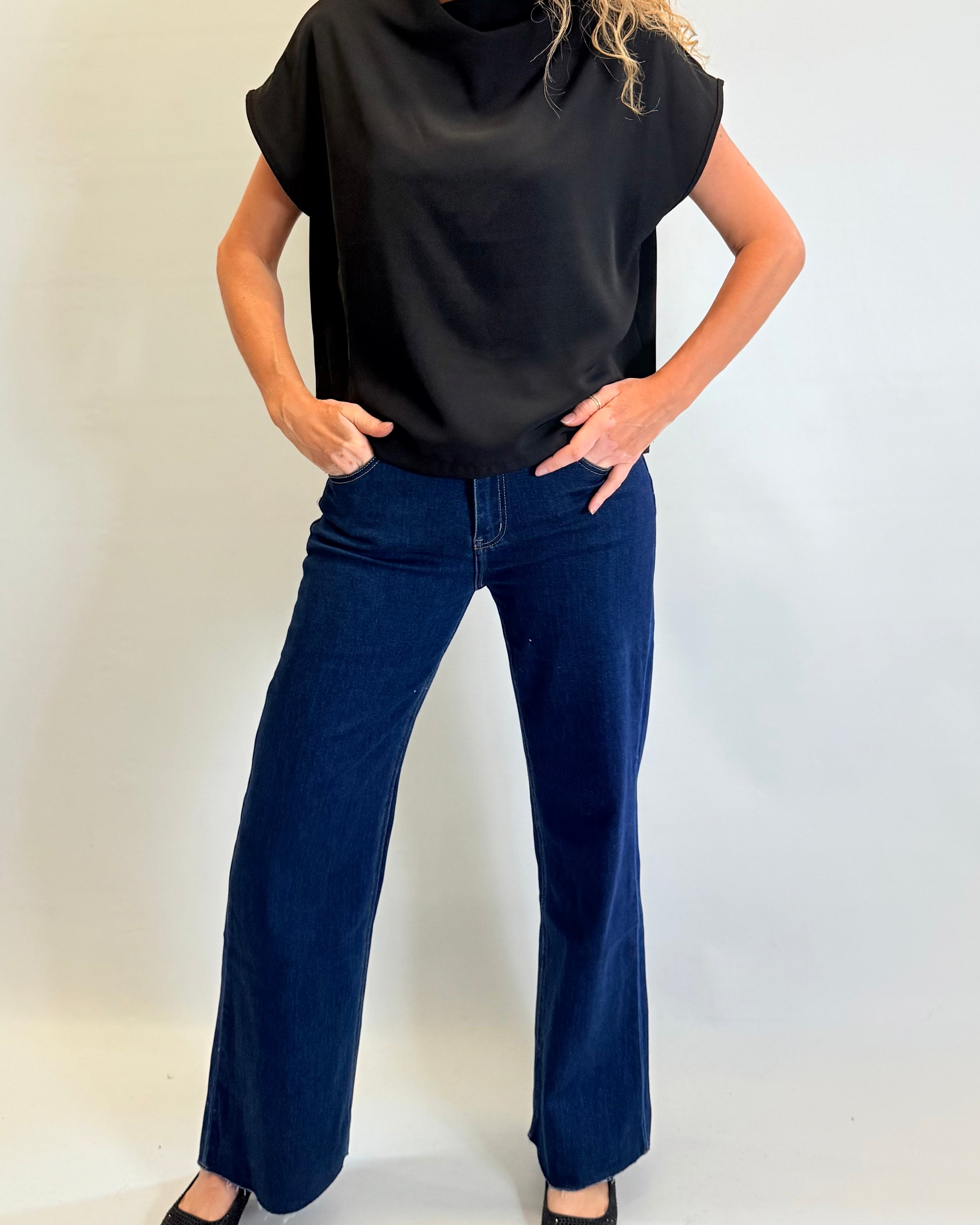 Person wearing a black sleeveless top and blue jeans against a white background