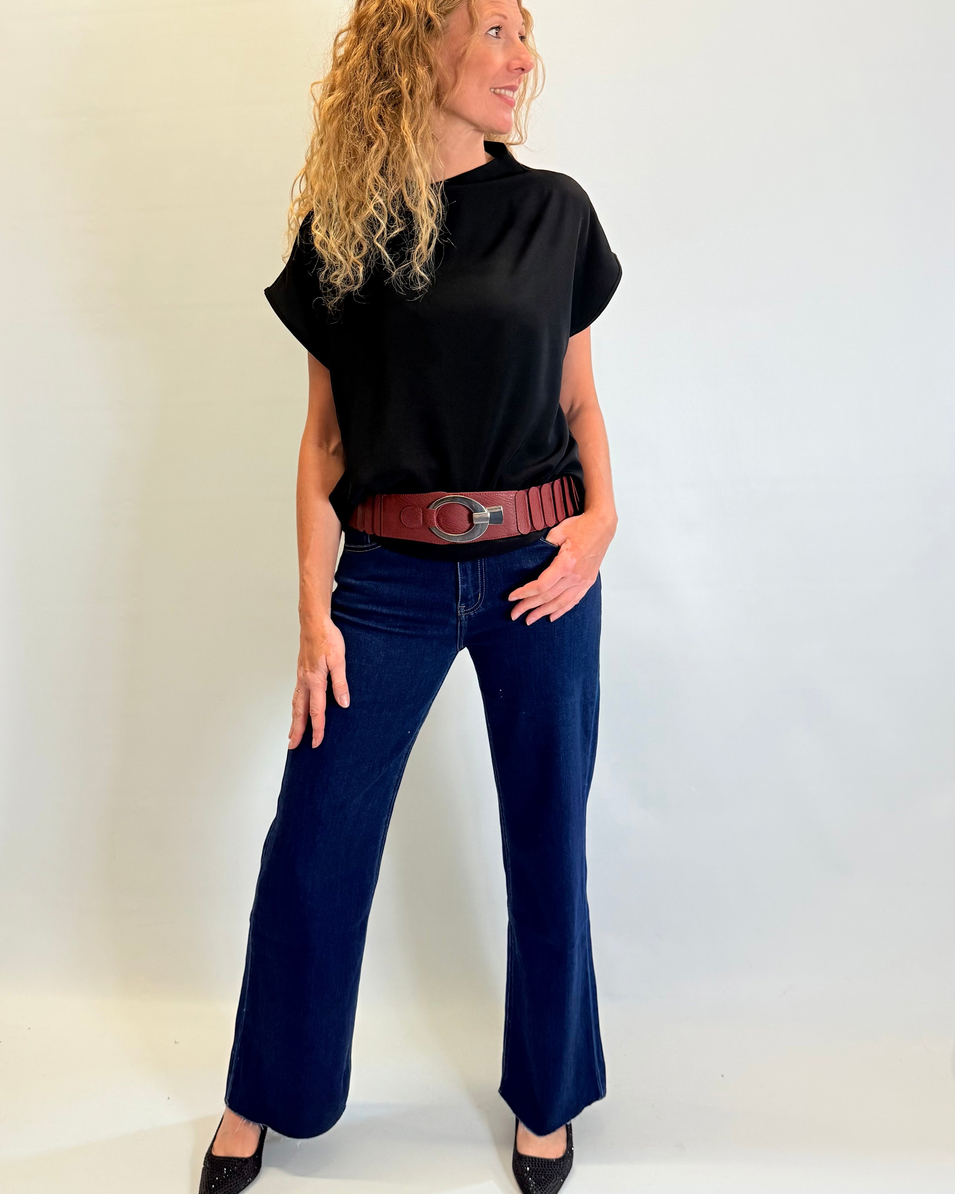 Woman wearing a black turtleneck, blue jeans, and a brown belt against a white background