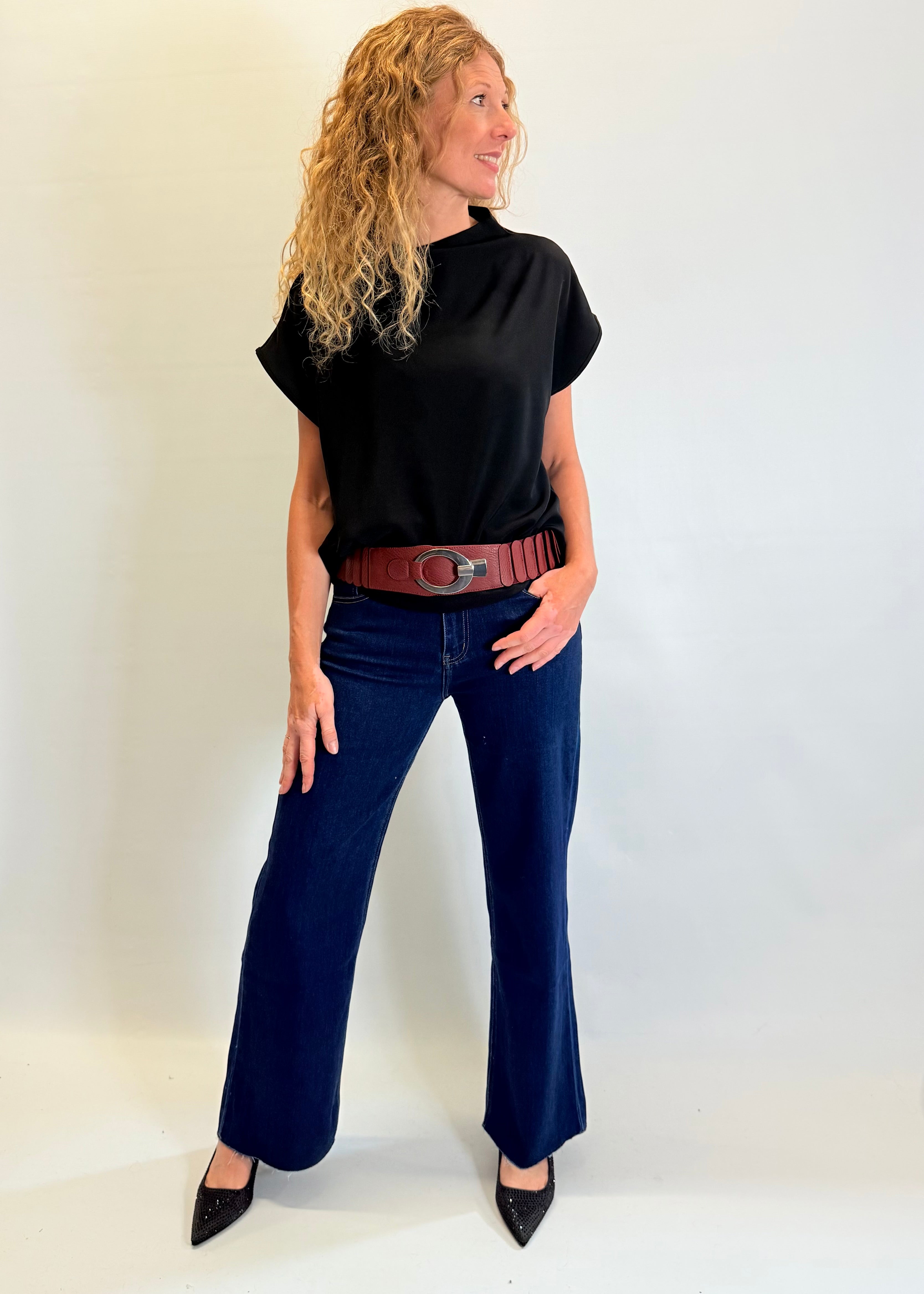 Woman wearing a black turtleneck, blue jeans, and a brown belt against a white background