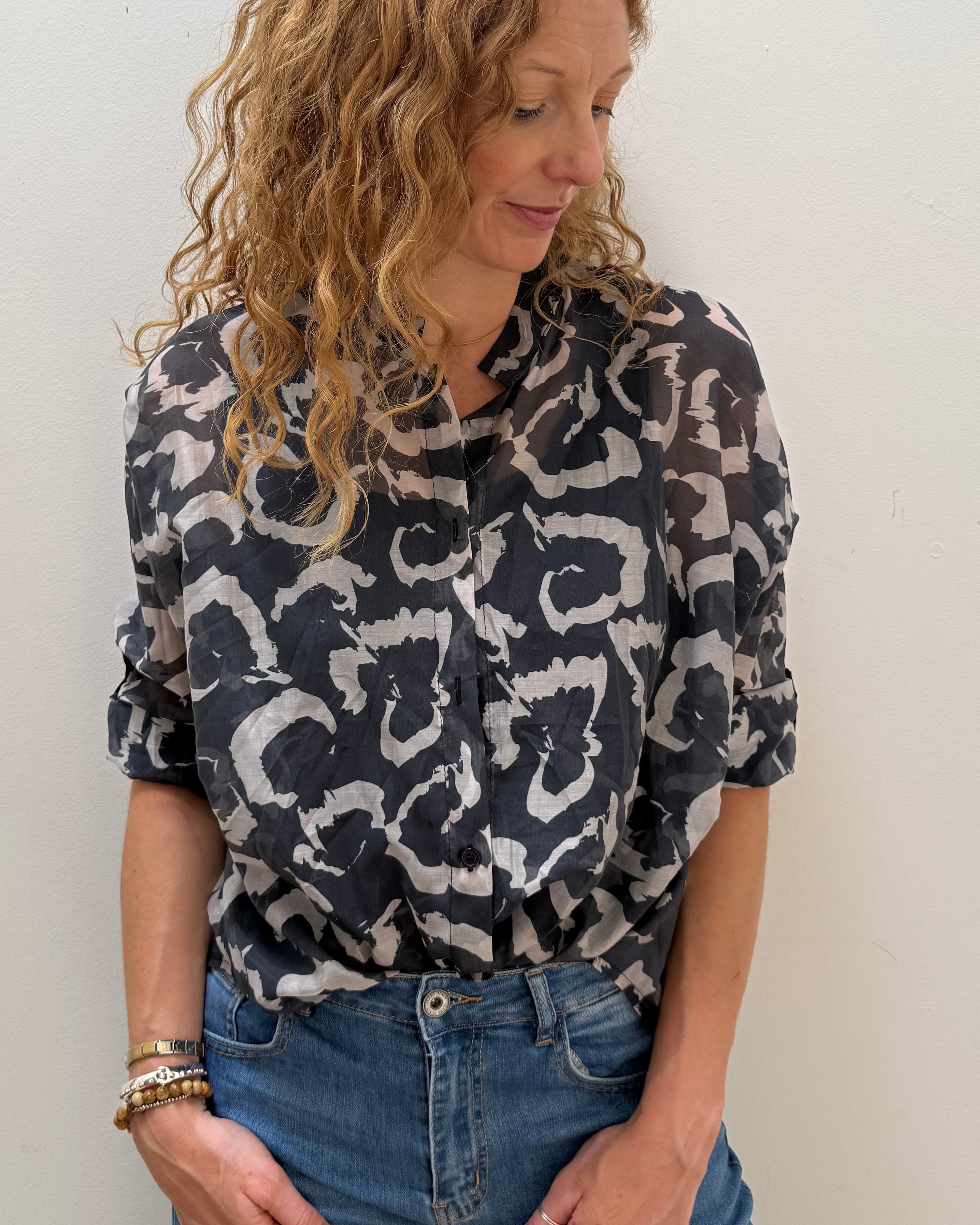 Woman wearing a patterned shirt and jeans against a white wall