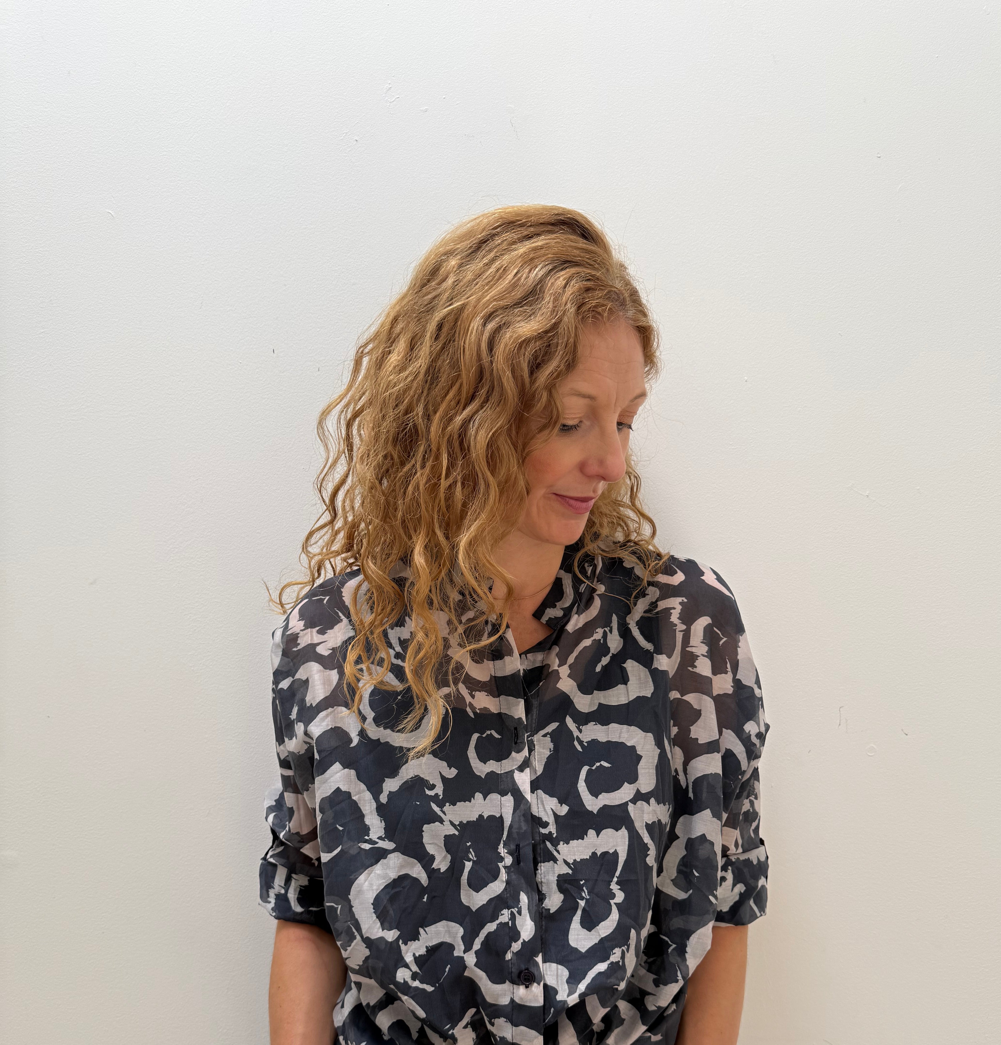 Woman wearing a patterned shirt and jeans against a white wall