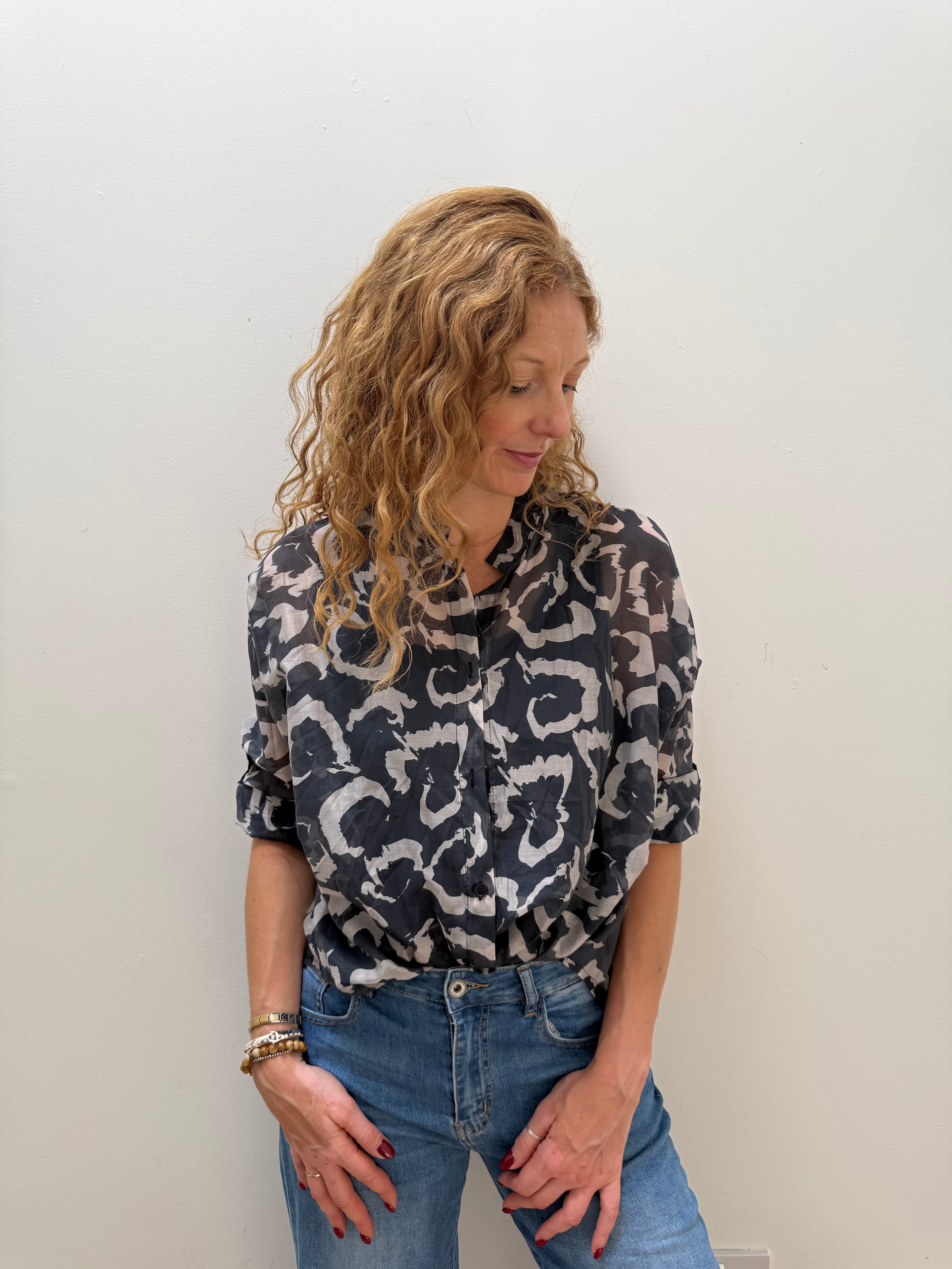 Woman wearing a patterned shirt and jeans against a white wall