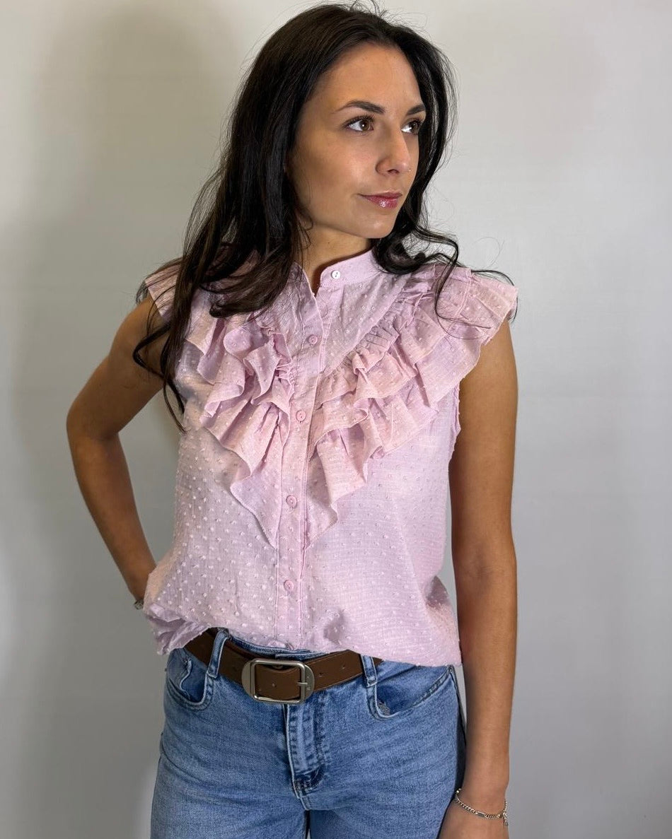 Woman wearing a light pink blouse with ruffles and blue jeans against a plain background