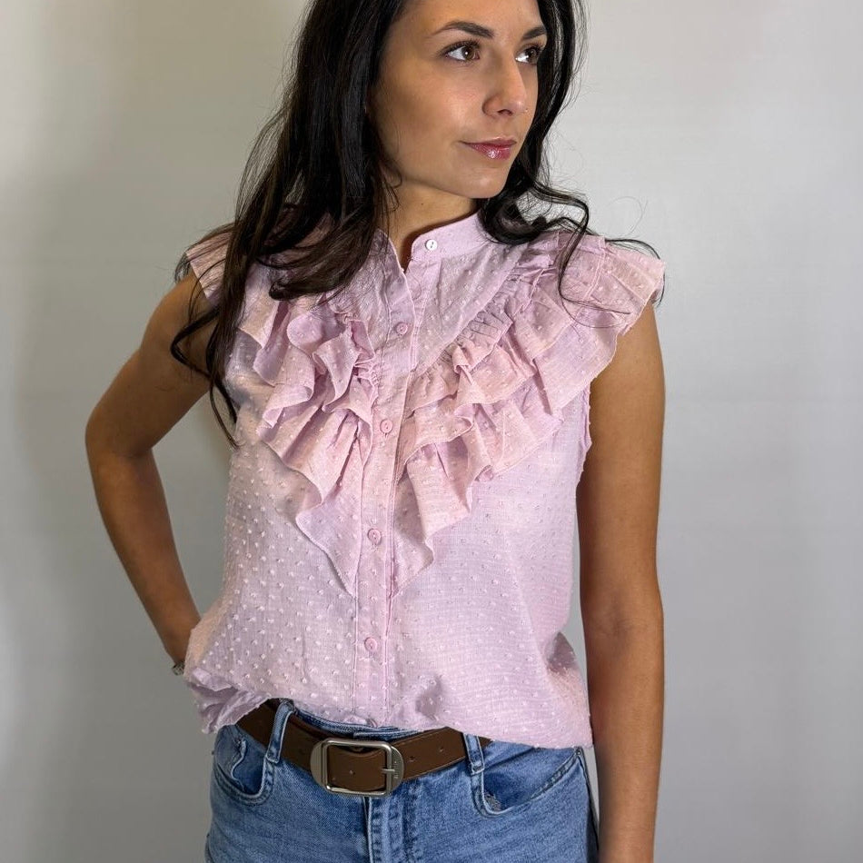 Woman wearing a light pink blouse with ruffles and blue jeans against a plain background