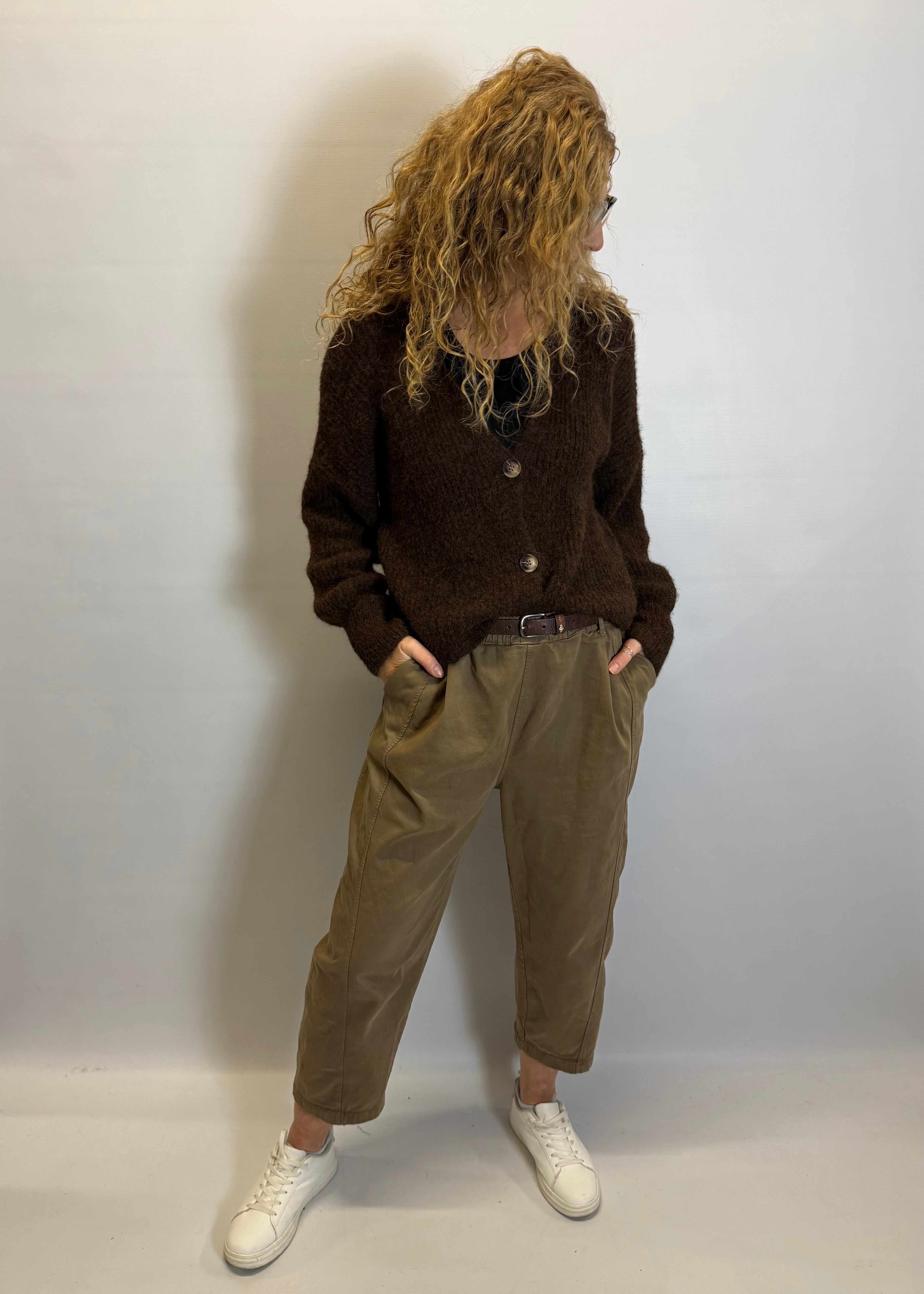 Person wearing a brown sweater and beige pants against a white background