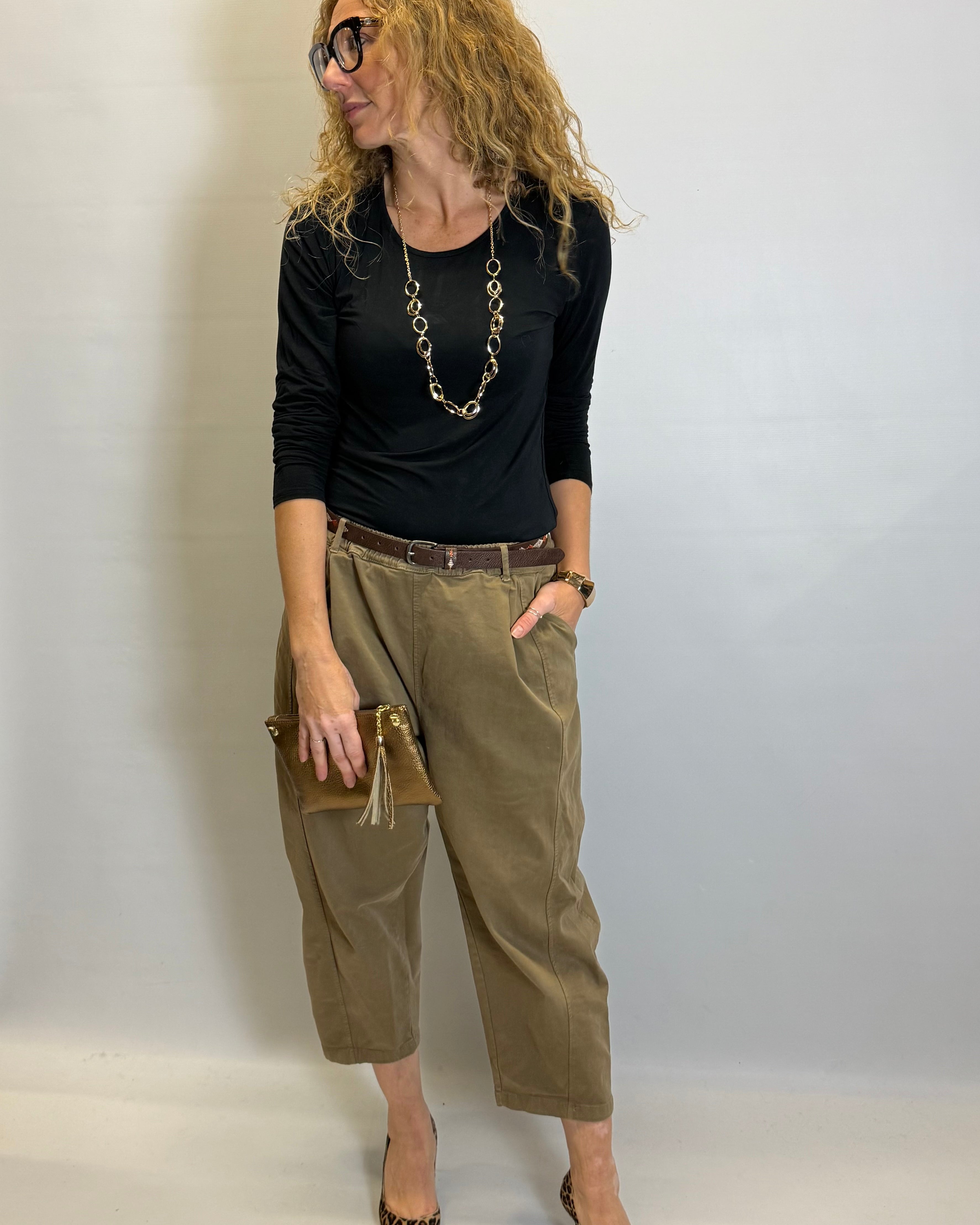 Woman wearing a black top, olive green pants, and leopard print shoes against a plain background