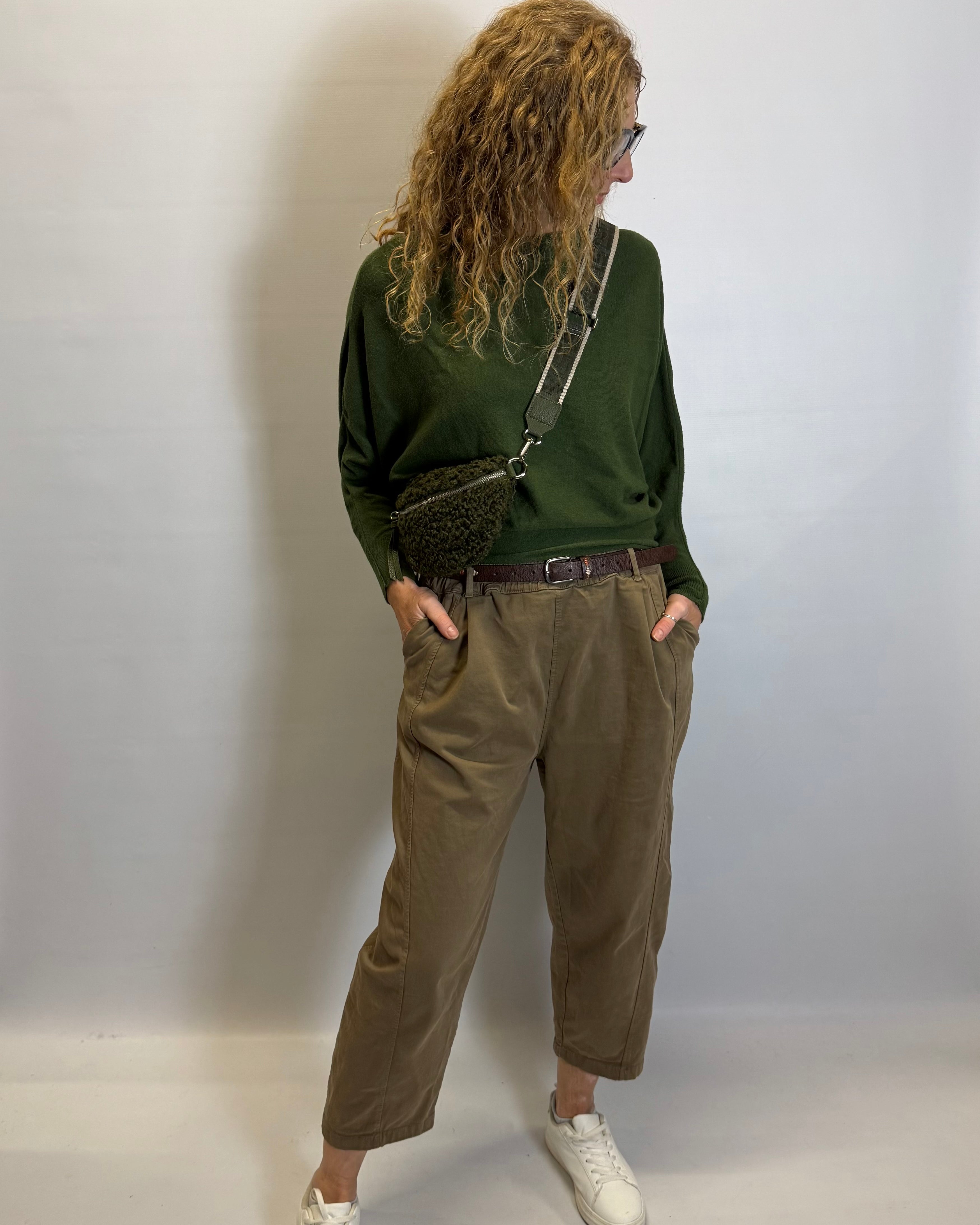 Person wearing a green sweater and brown pants against a plain background