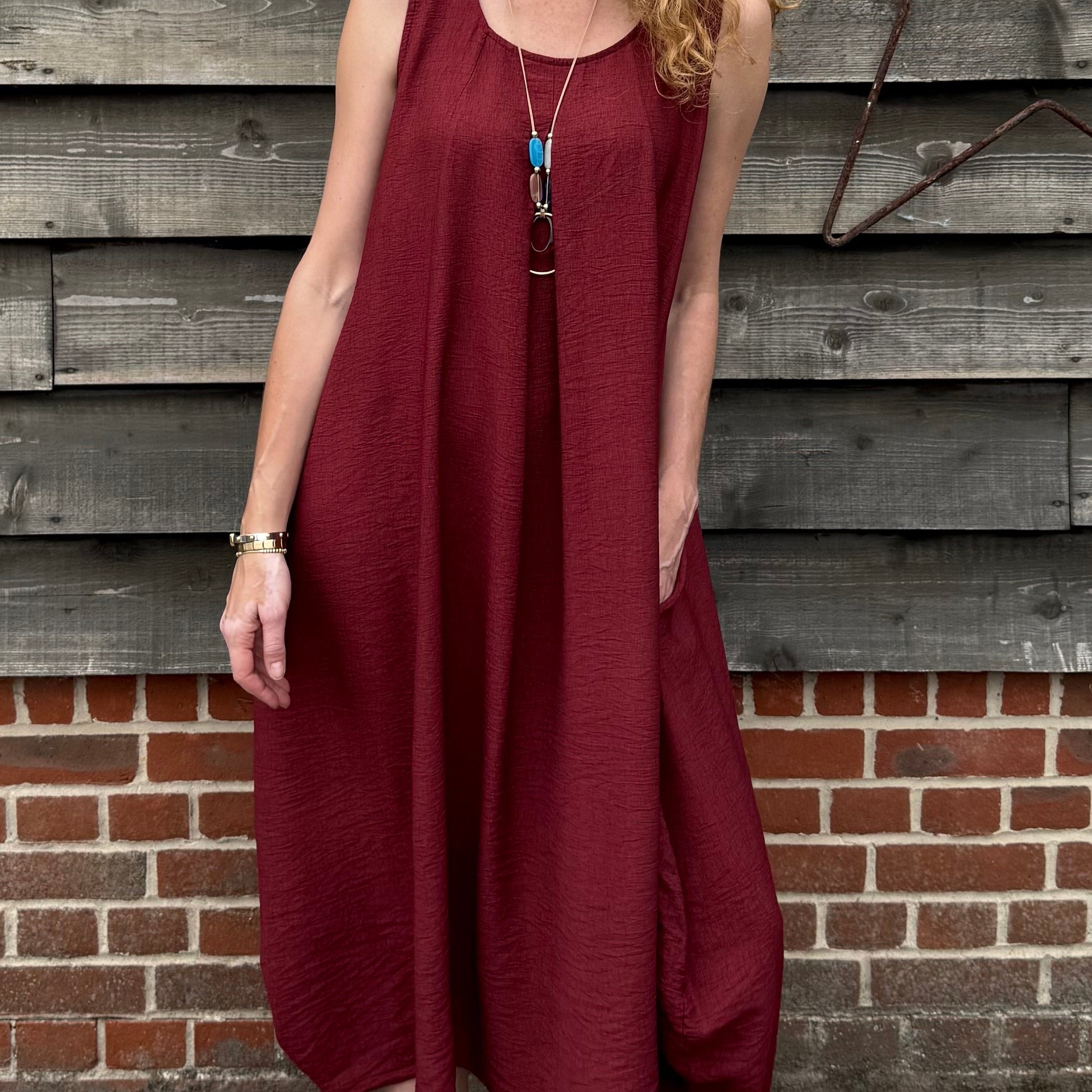 Woman in a burgundy dress standing against a wooden wall.