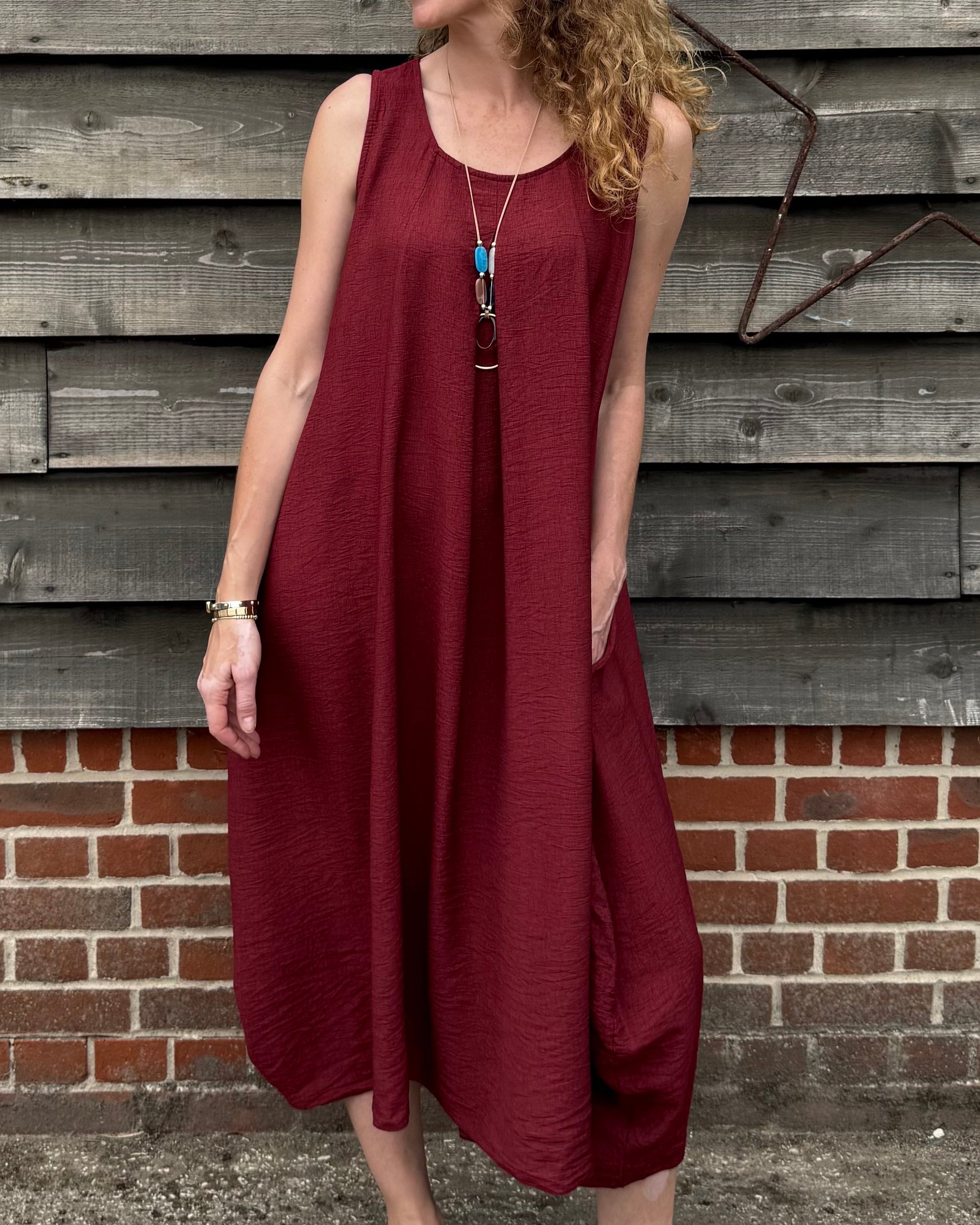 Woman in a burgundy dress standing against a wooden wall.