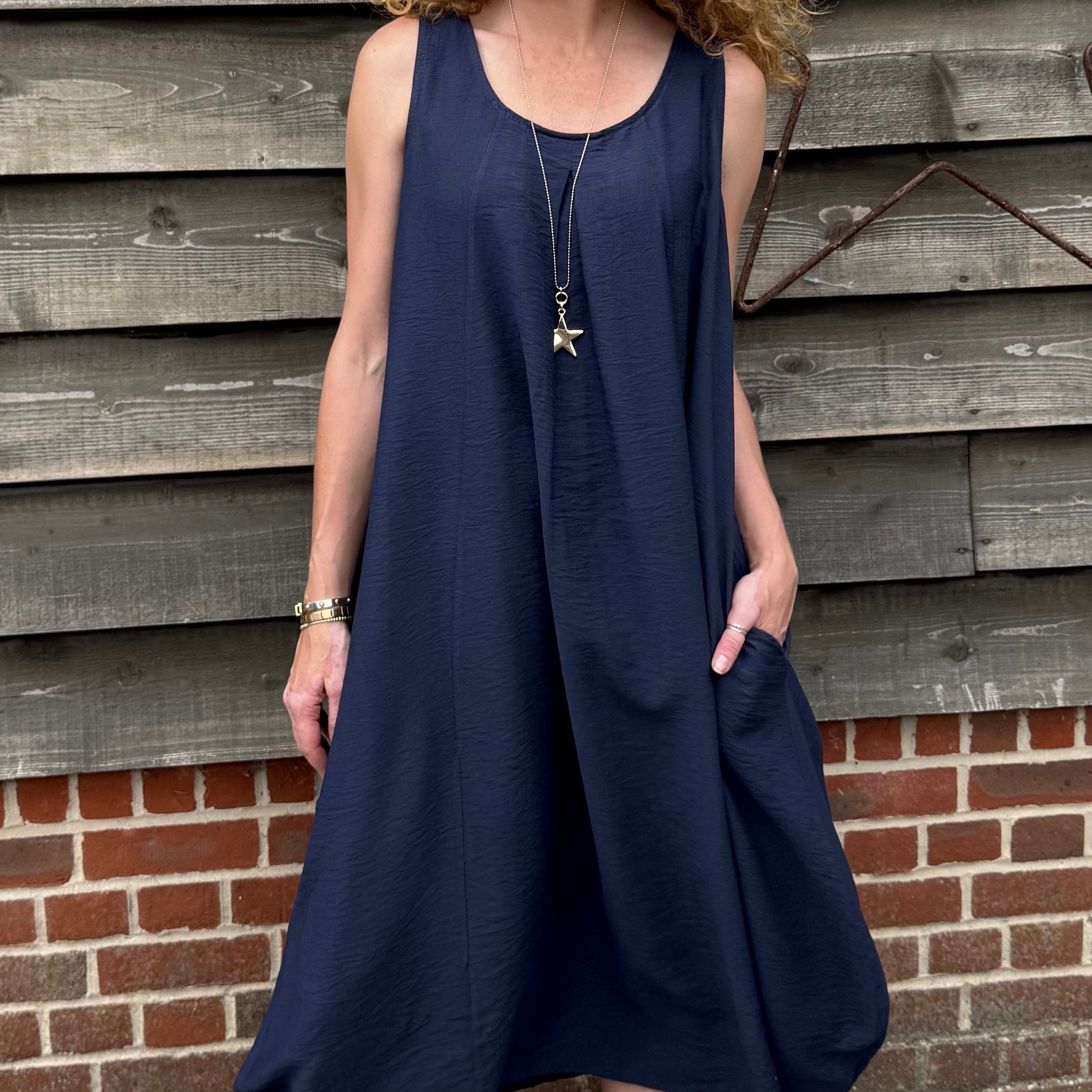 Woman wearing a navy blue dress standing against a wooden wall.