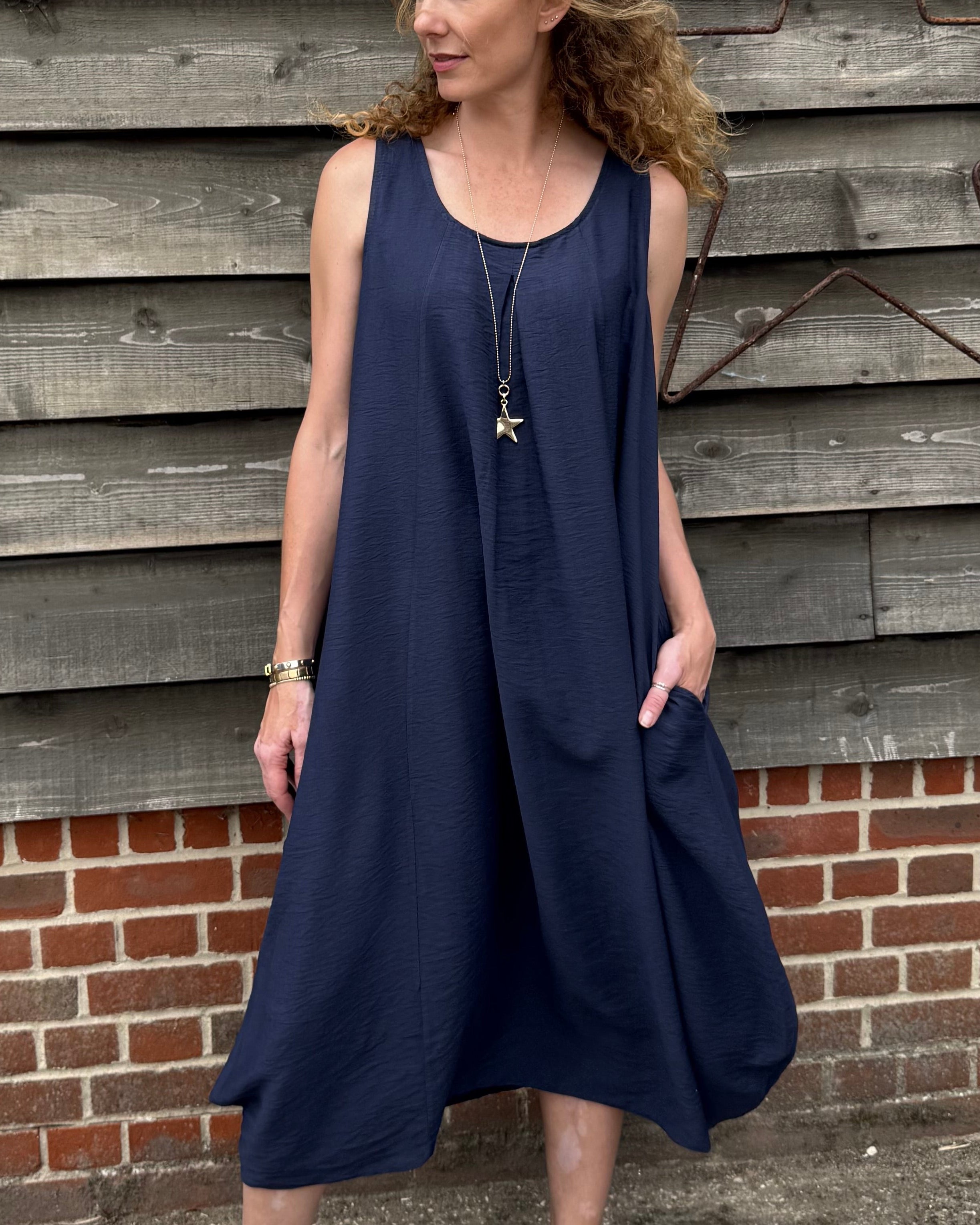 Woman wearing a navy blue dress standing against a wooden wall.