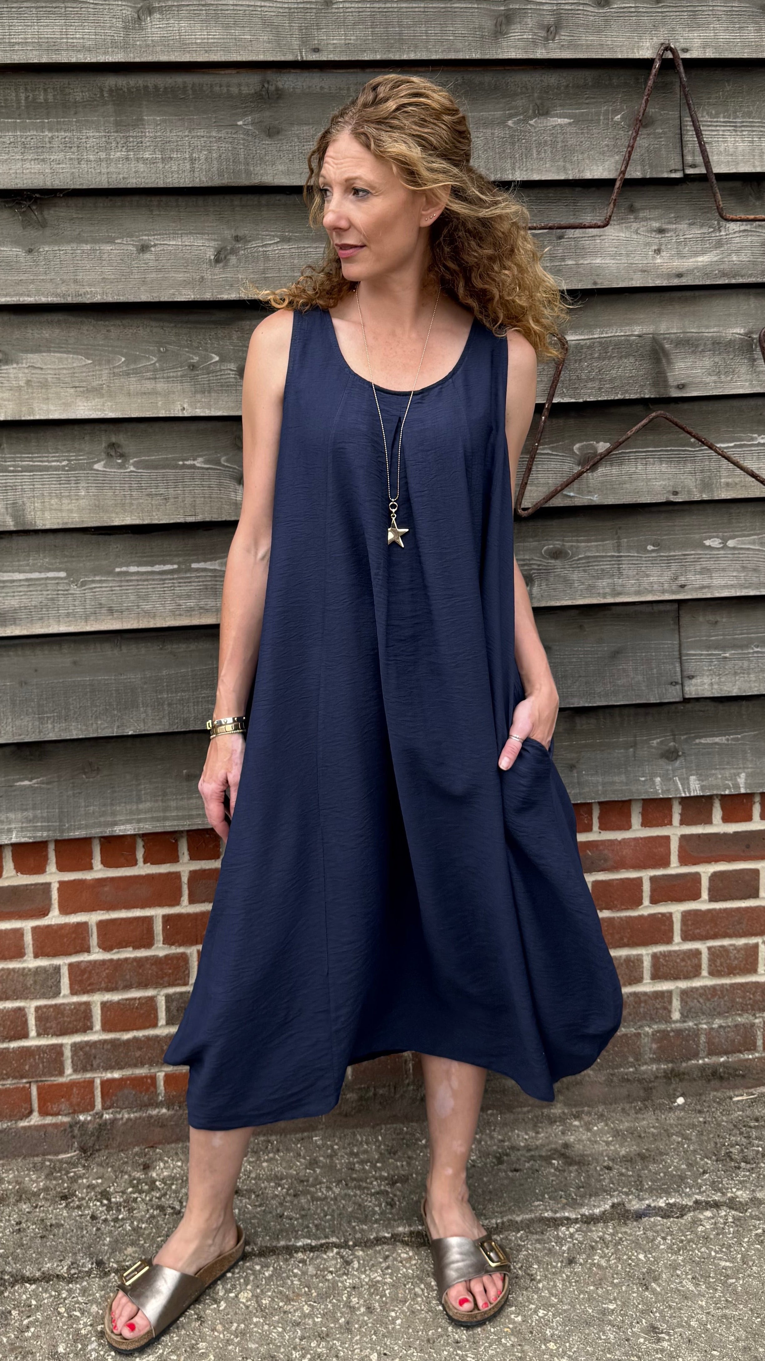 Woman wearing a navy blue dress standing against a wooden wall.