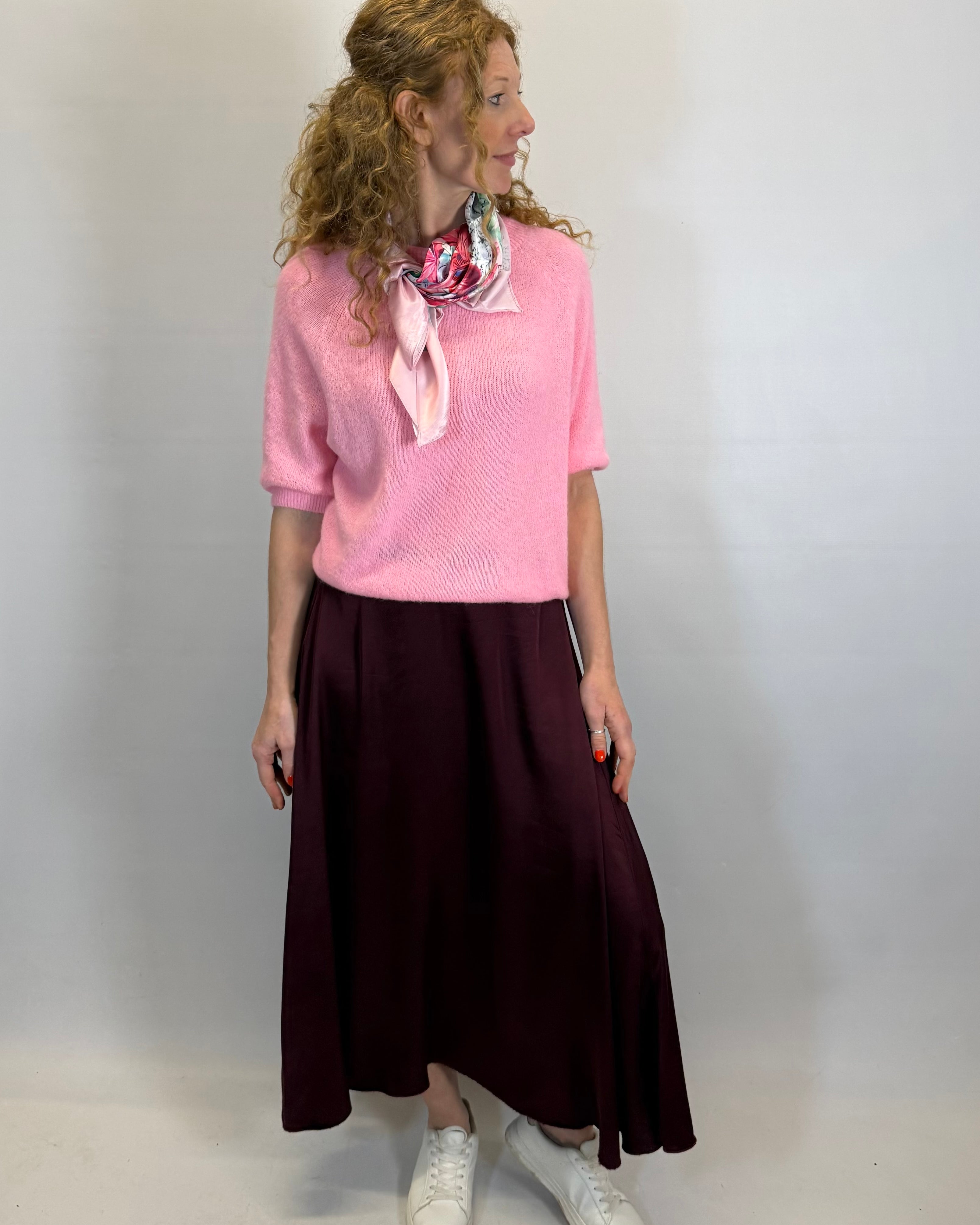 Woman wearing a pink sweater and dark skirt with a white background