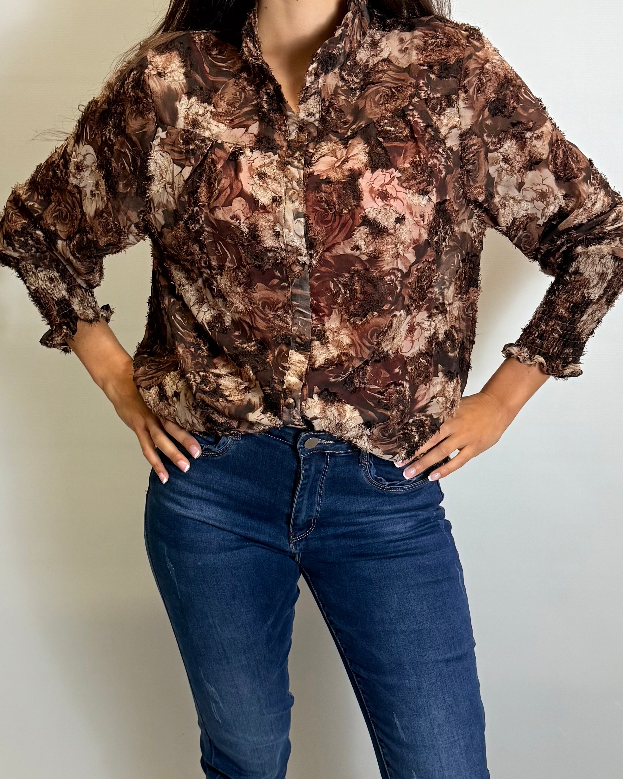 Person wearing a patterned shirt and blue jeans against a plain background