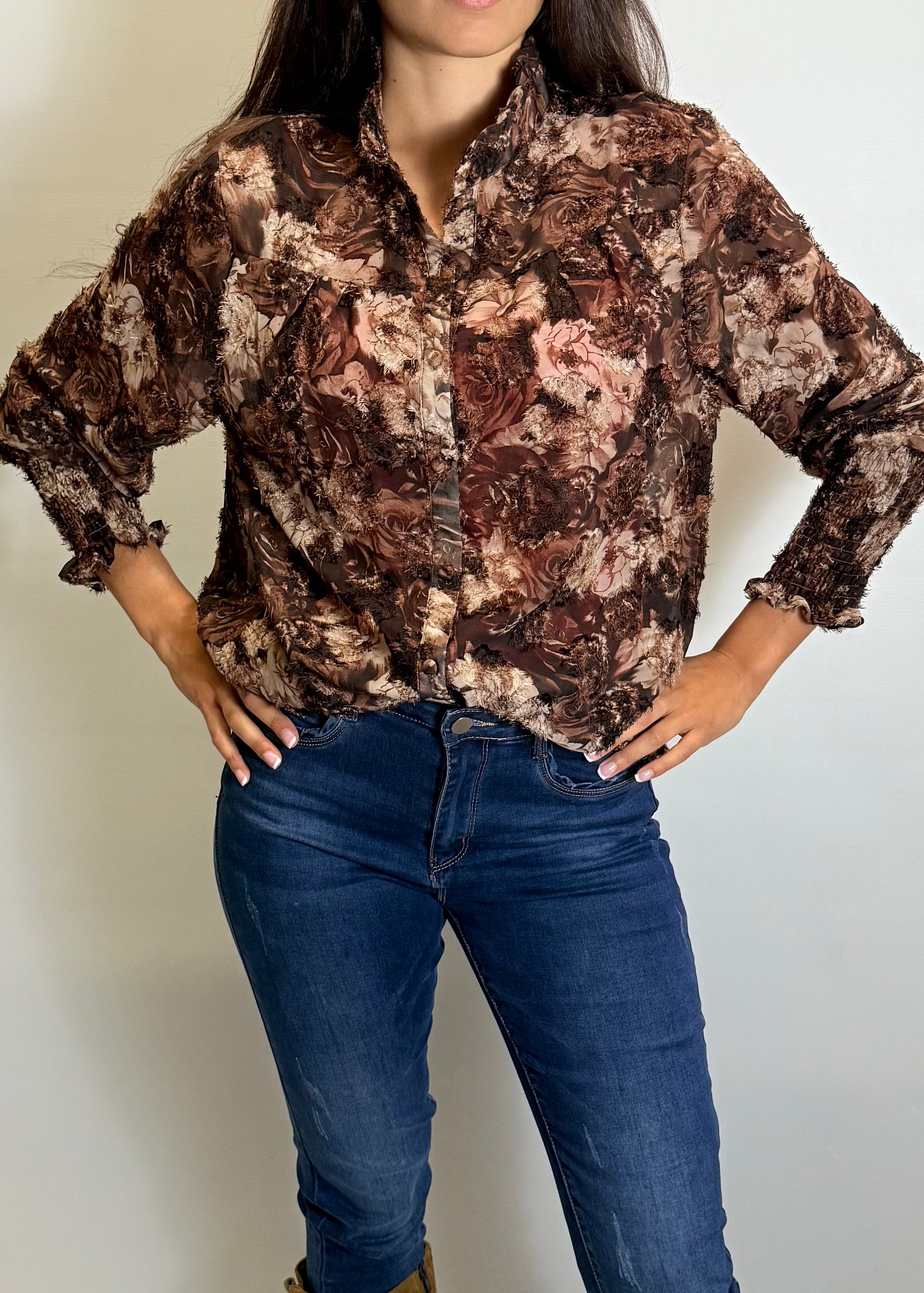 Person wearing a patterned shirt and blue jeans against a plain background