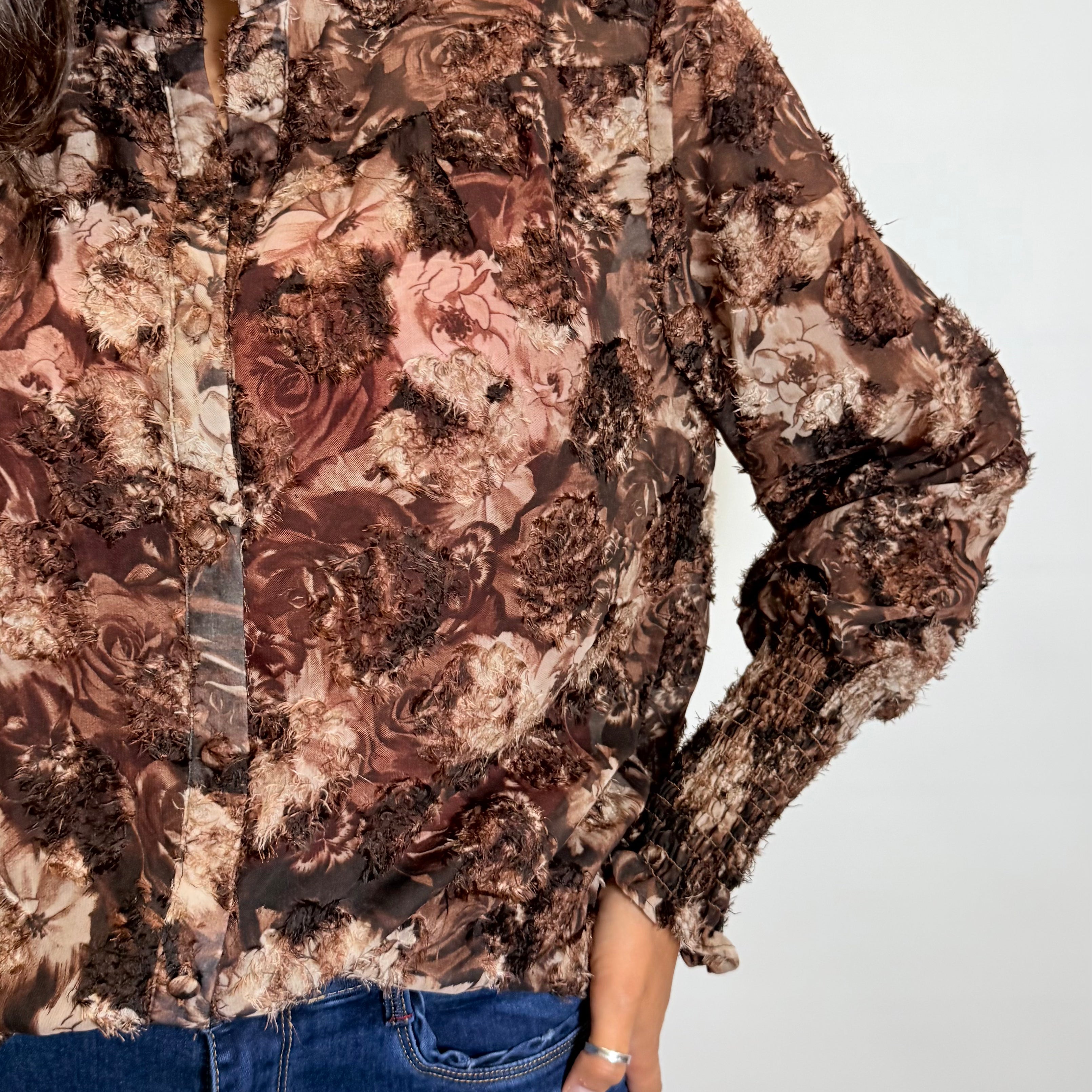 Person wearing a floral patterned blouse with long sleeves on a plain background
