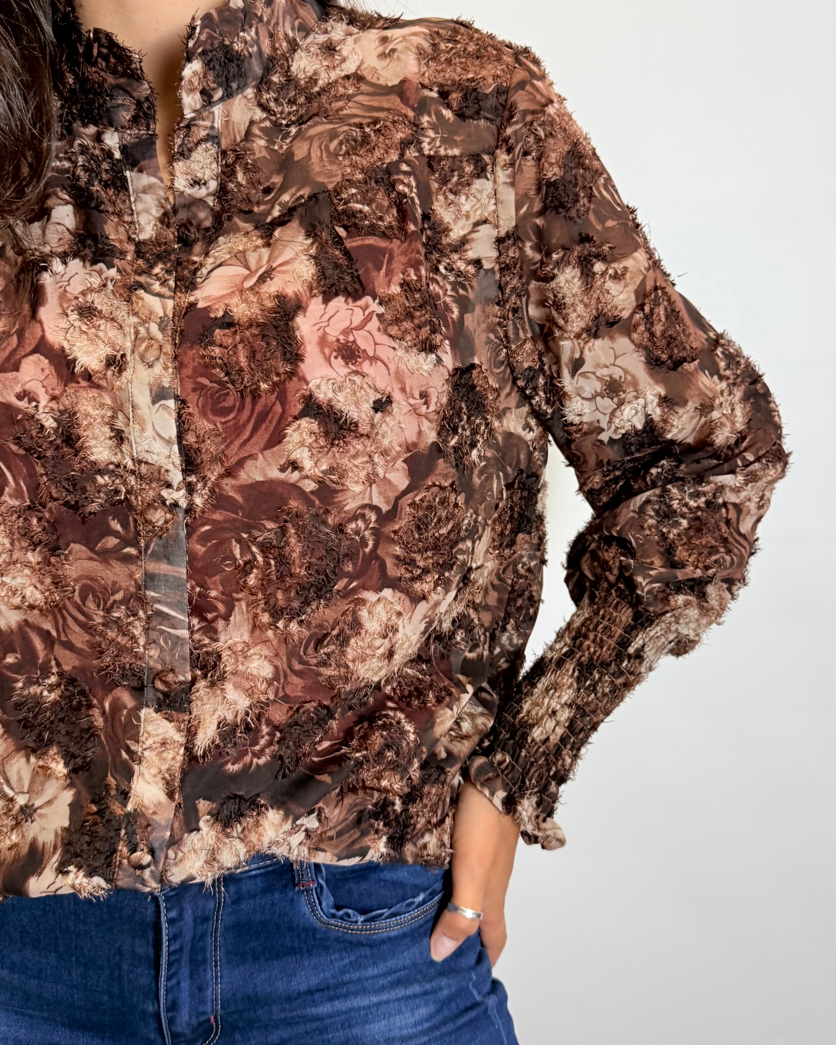Person wearing a floral patterned blouse with long sleeves on a plain background