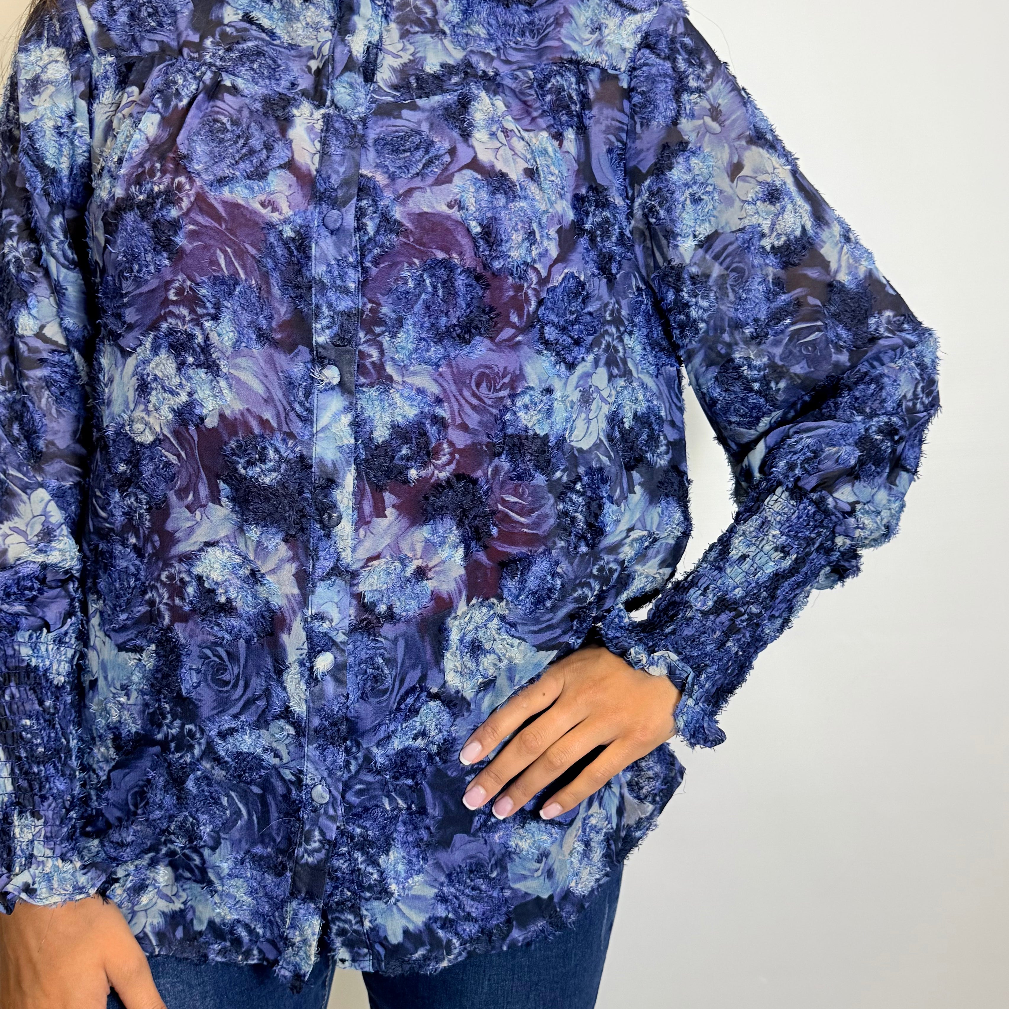 Woman wearing a blue floral blouse, jeans, and brown boots against a plain background