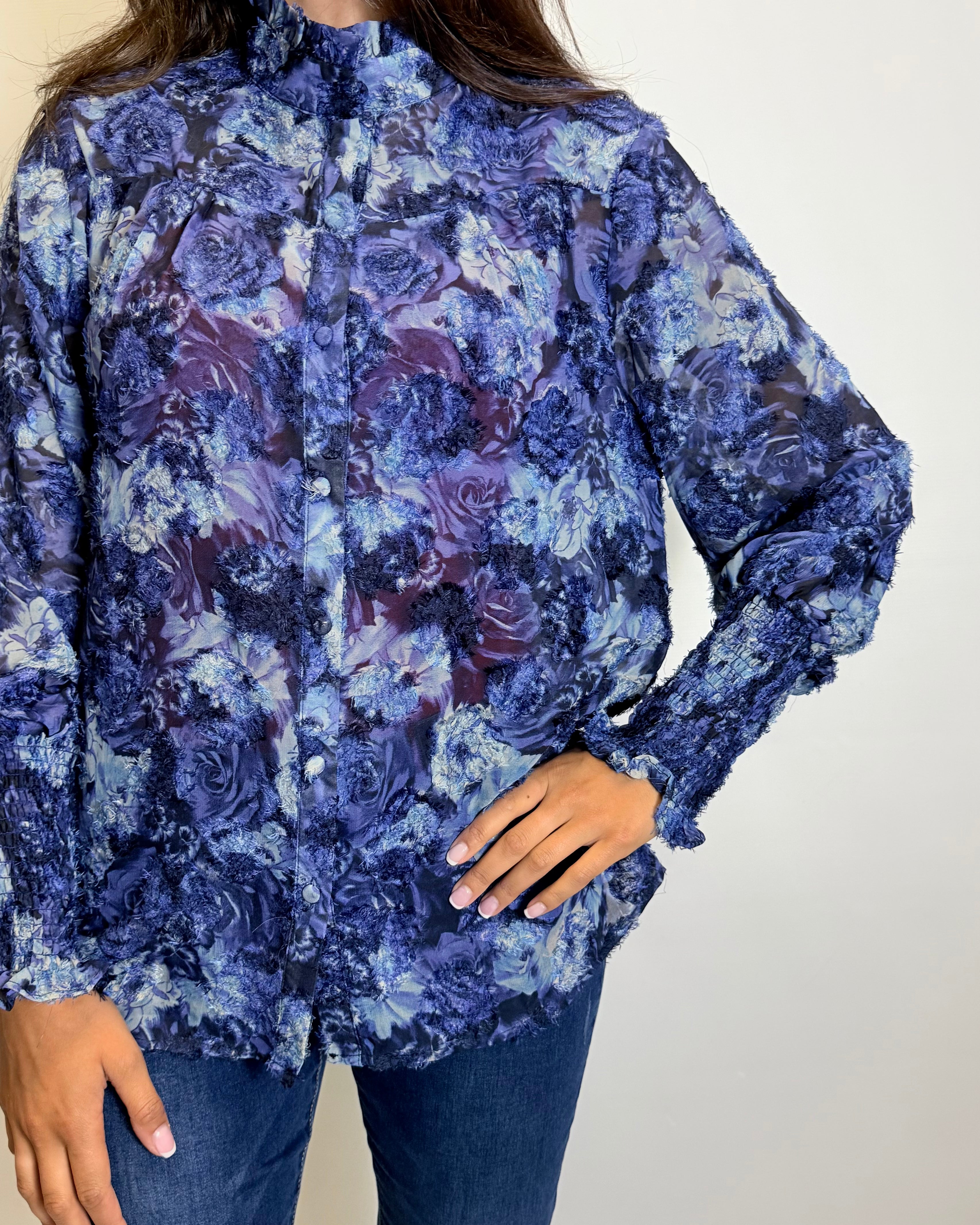 Woman wearing a blue floral blouse, jeans, and brown boots against a plain background