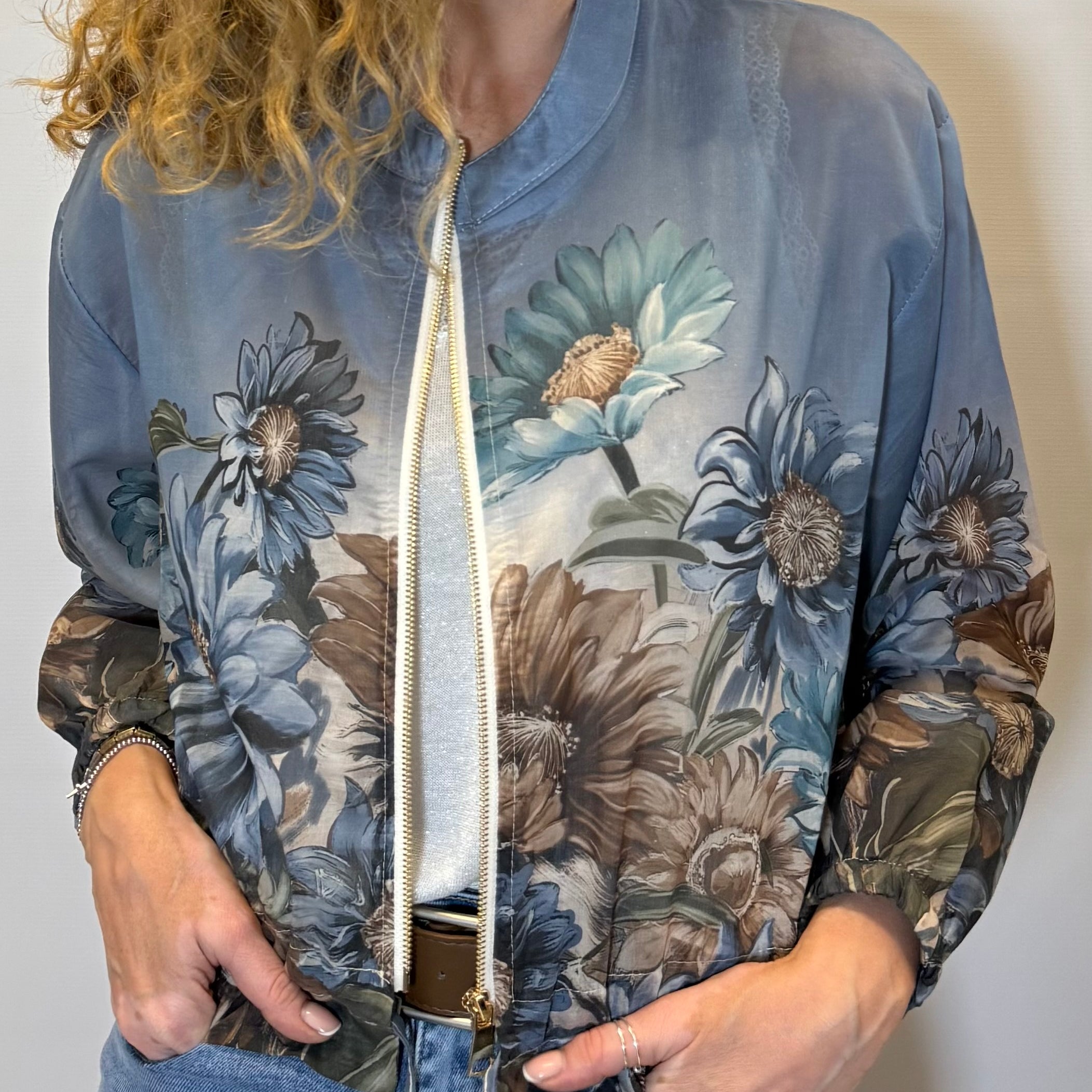 Woman wearing a floral-patterned bomber jacket against a plain background
