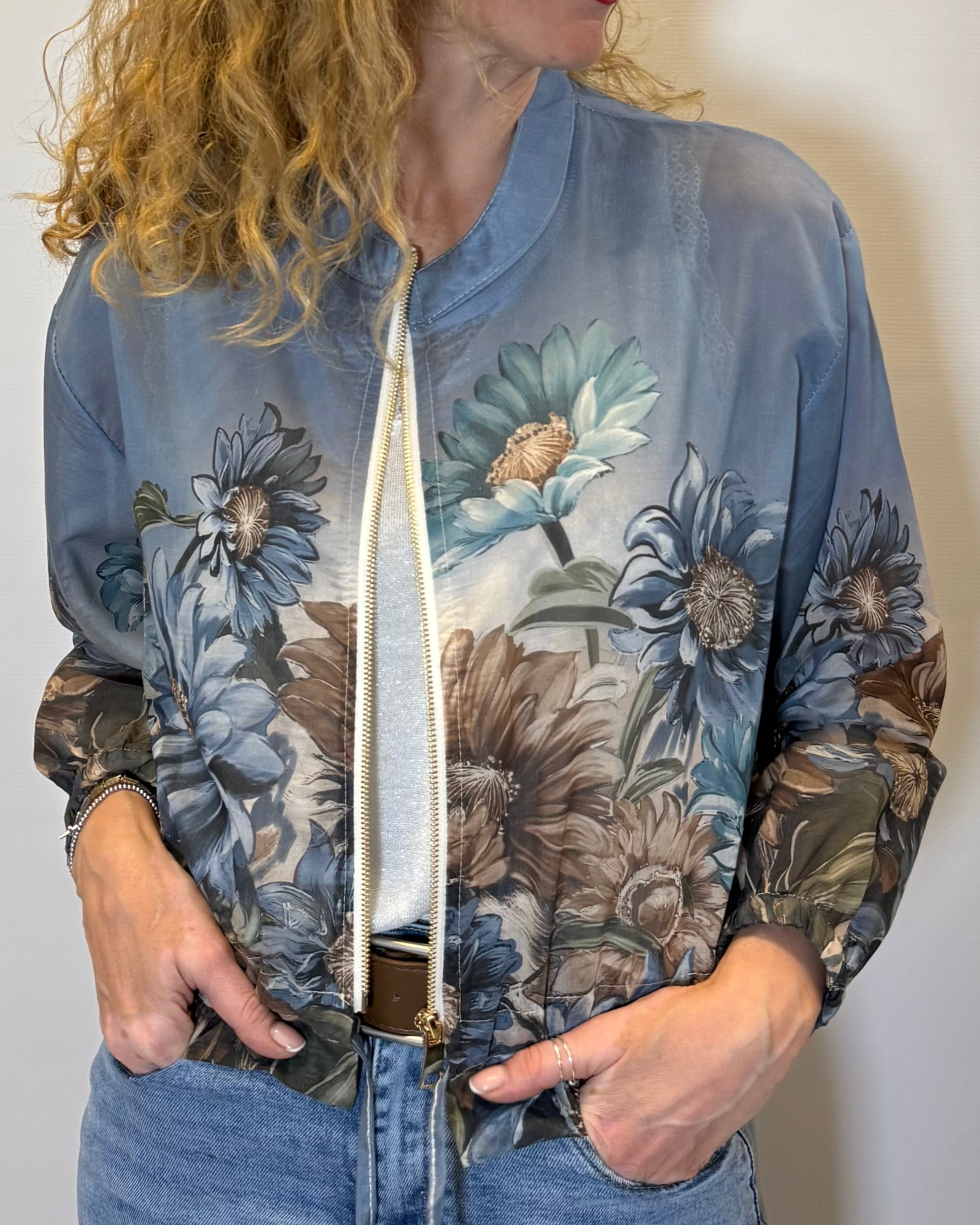 Woman wearing a floral-patterned bomber jacket against a plain background