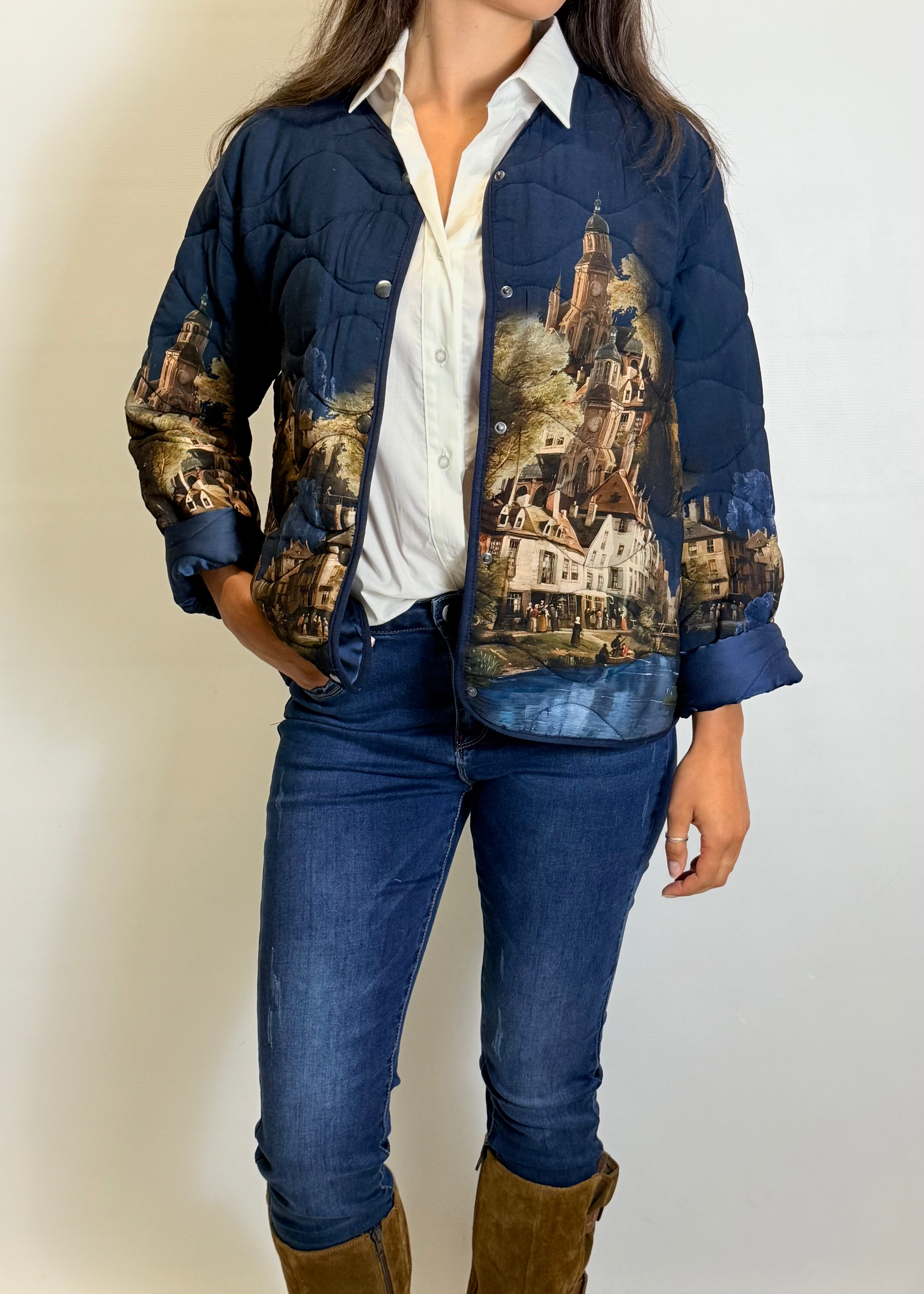 Person wearing a blue jacket with artistic designs, white shirt, blue jeans, and brown boots on a plain background